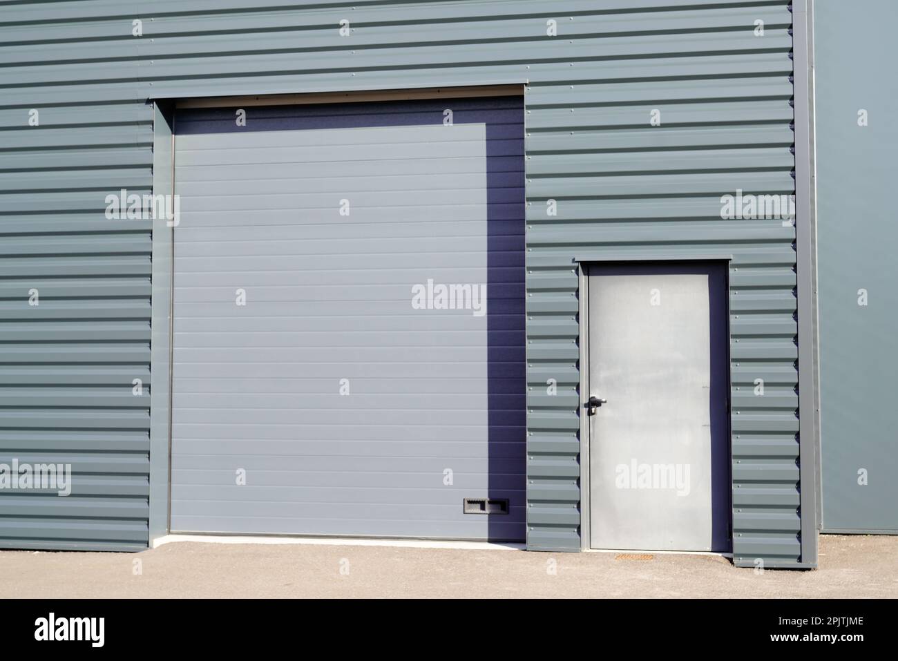 grey metal roll-down shutters on vertical profiled sheeting gray new industrial building Stock Photo