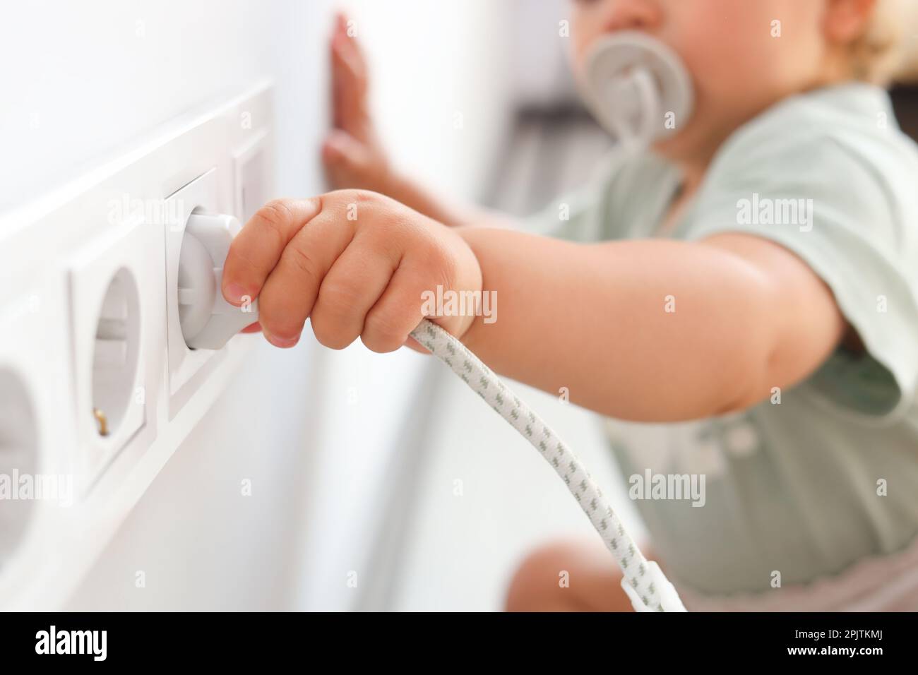 Cute baby playing with plug and electrical socket at home, closeup