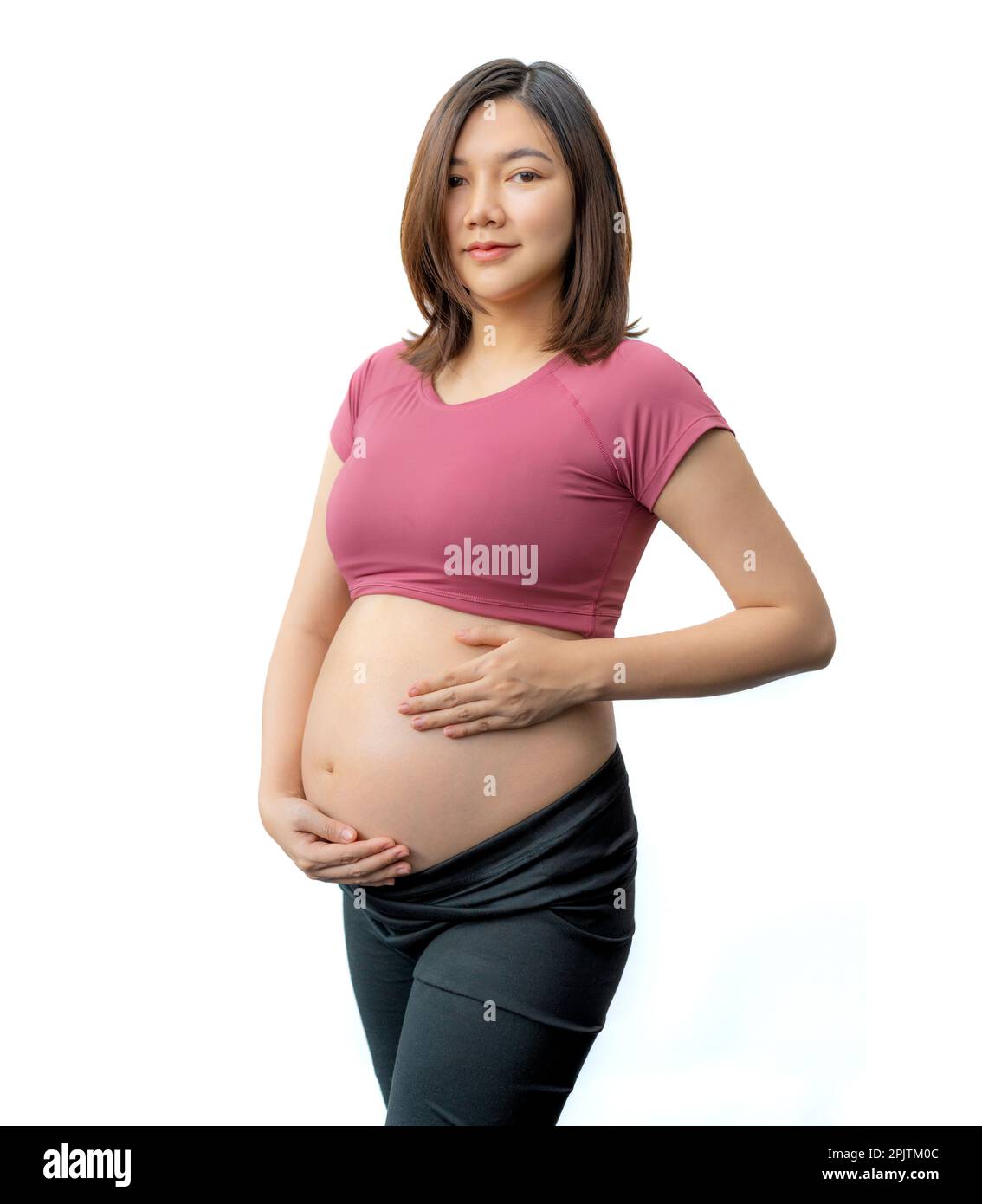 Happy pregnant woman in fitness clothes standing holding her exposed belly against white background, room for copy space Stock Photo
