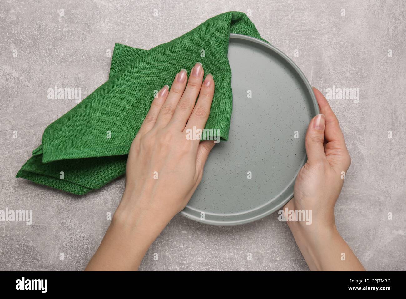 Woman wiping plate at light grey table, top view Stock Photo