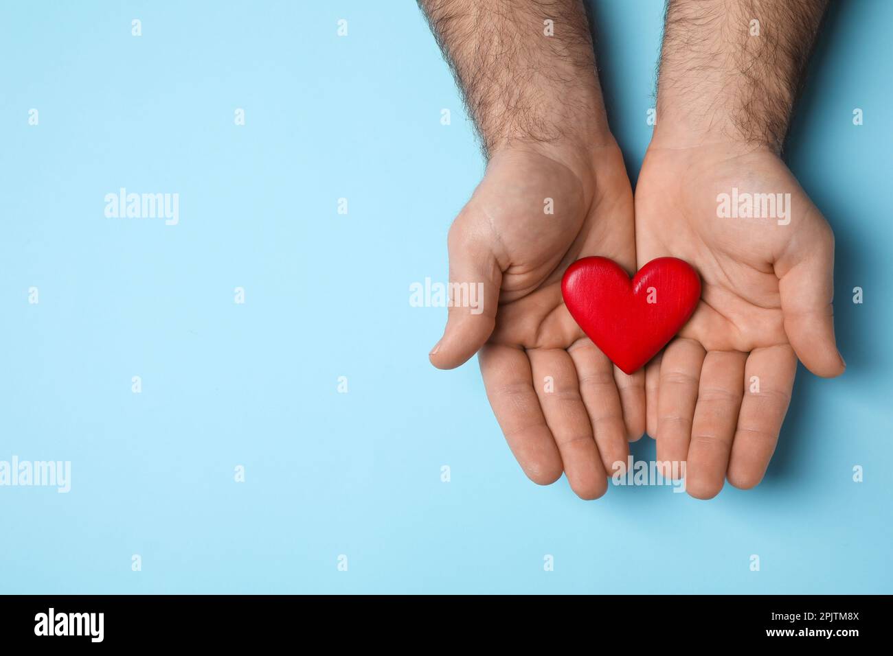 Man holding red heart on light blue background, top view. Space for ...