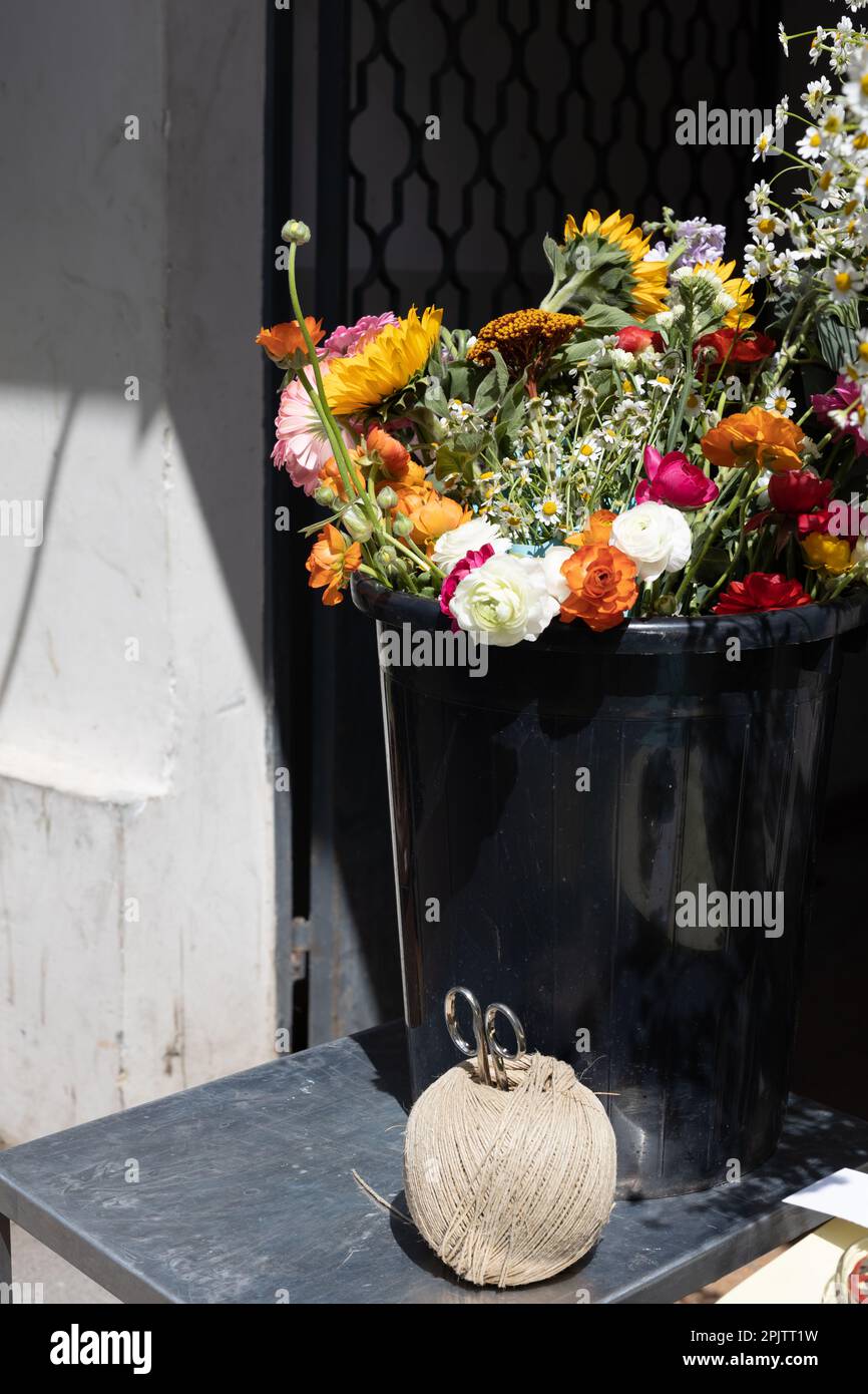 Bouquet of sunflower, ranunculus, ranunculus and daisies in a black plastic bucket for sale