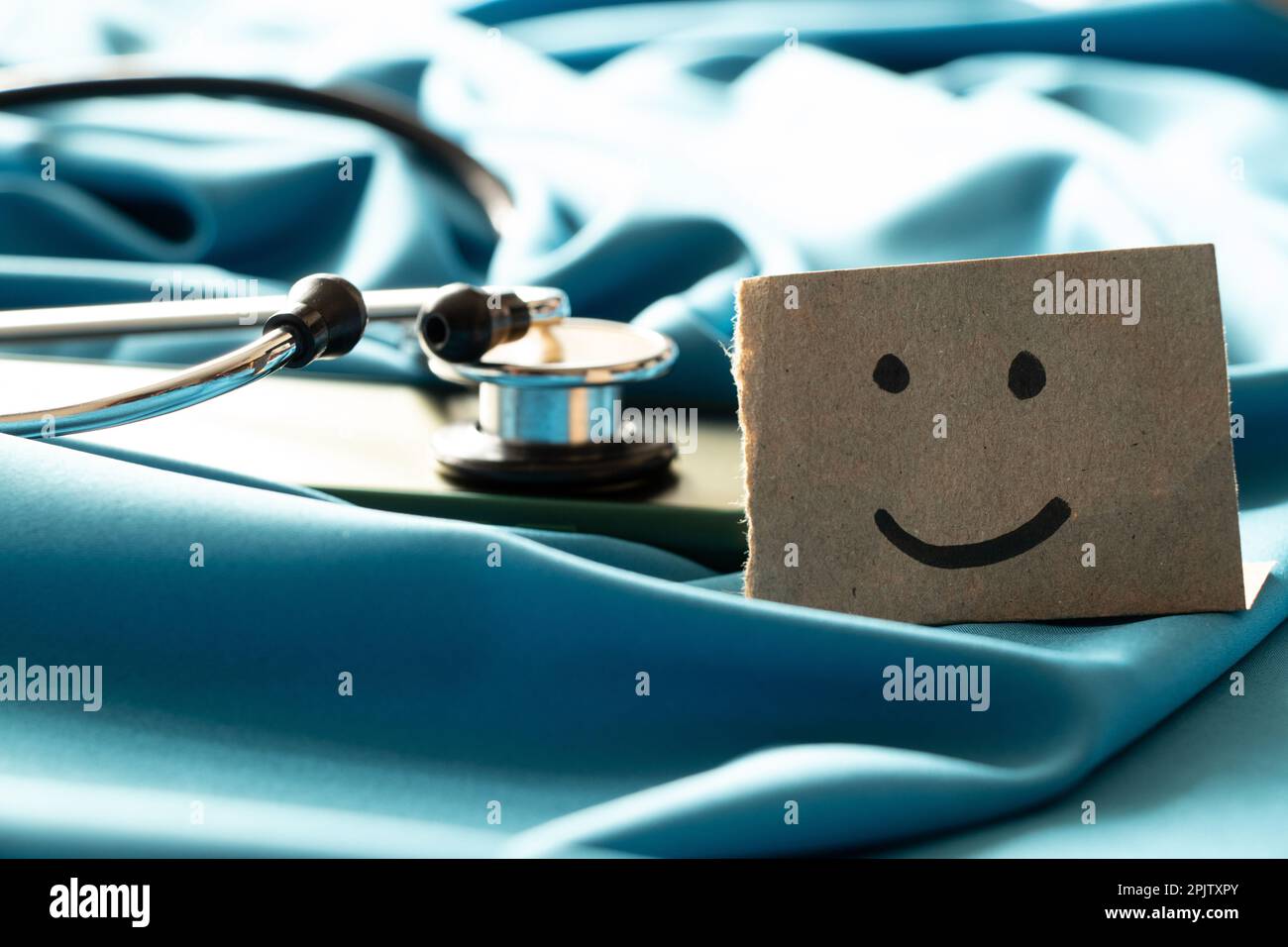 A stethoscope lies on a smartphone on a blue background and next to it is a paper card with a drawn smile, an online doctor Stock Photo