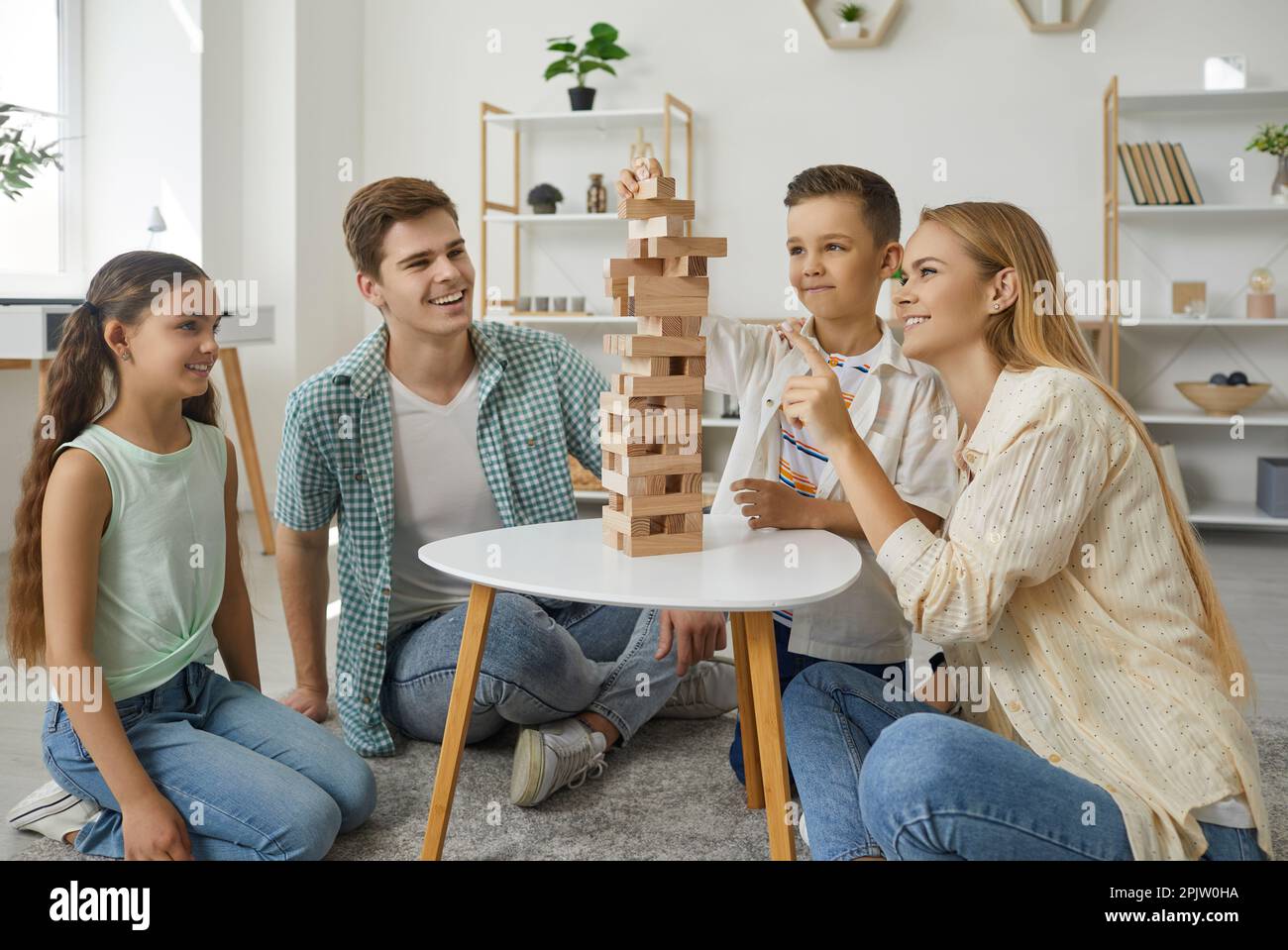 Friendly happy family with two children playing tumbling tower sitting on floor at home living room. Stock Photo