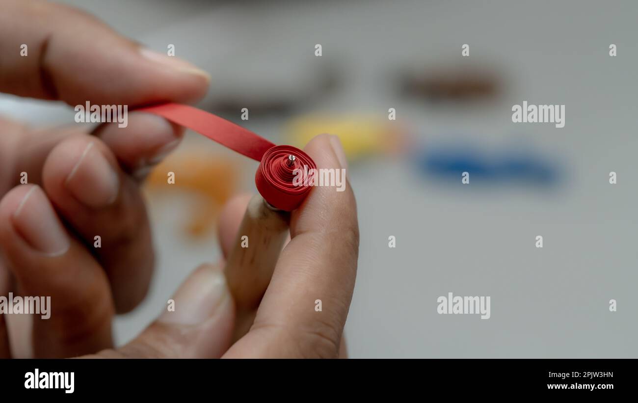 Close up of a woman's hands sewing a red paper stripes to make crafts on a white background Stock Photo