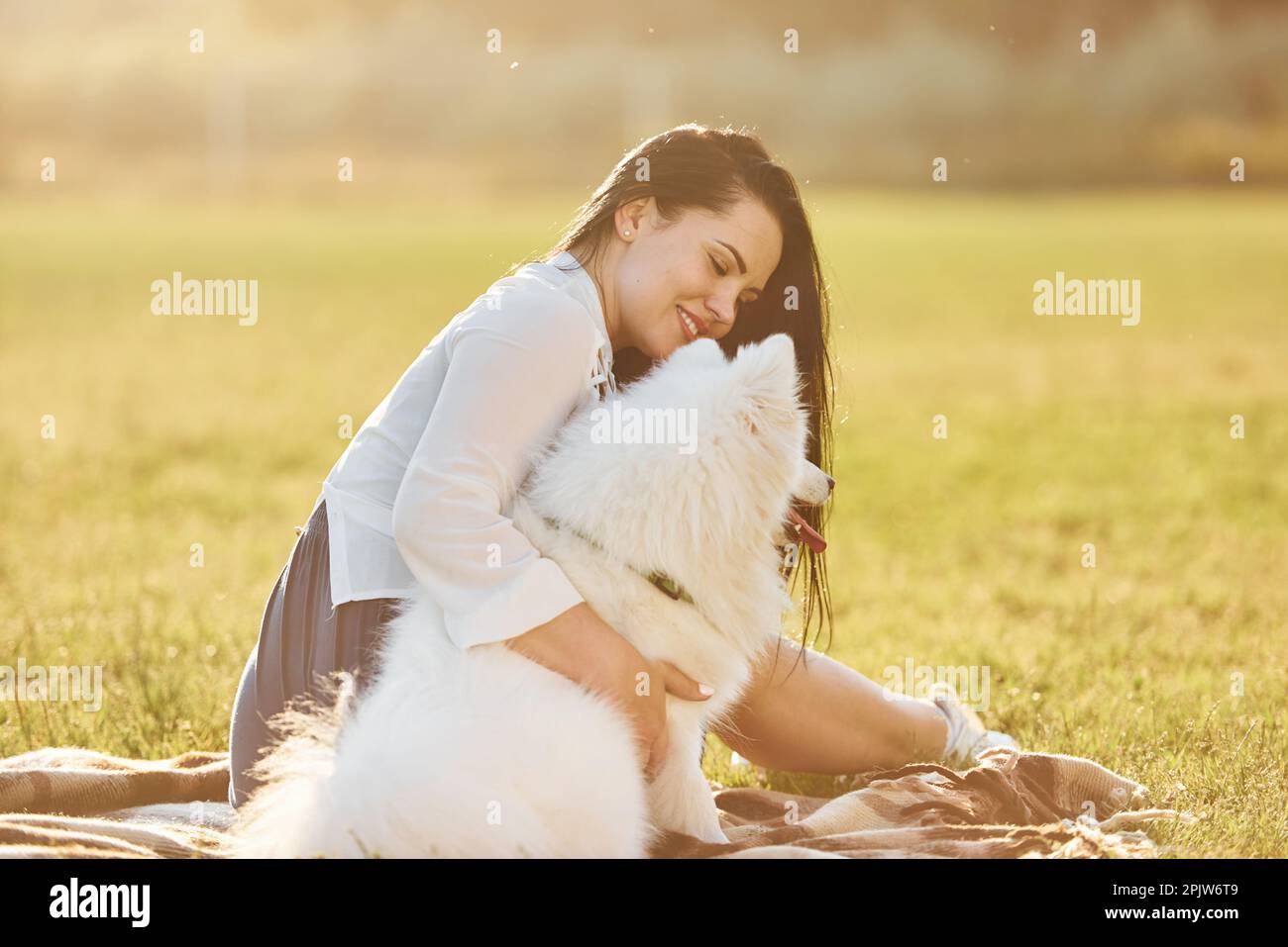 Beautiful woman in white shirt sitting with her dog on the field at ...