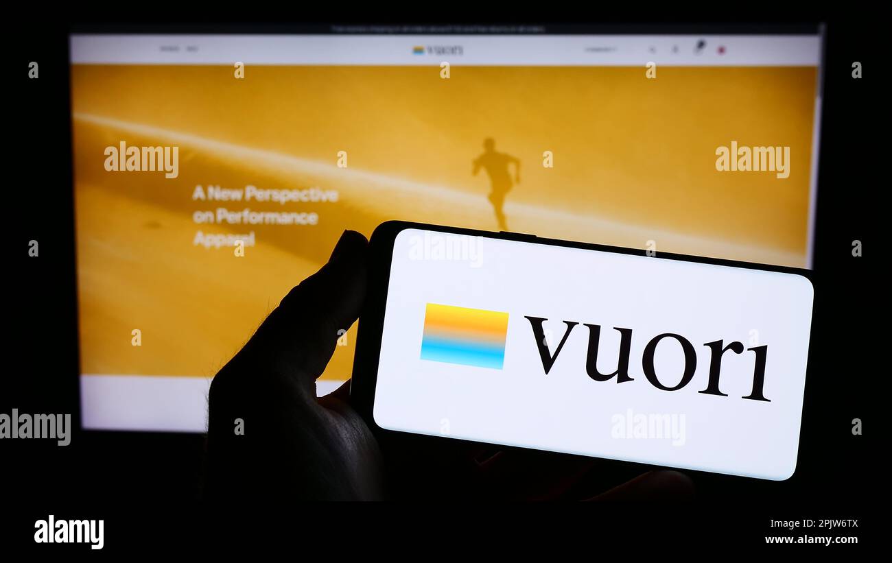Person holding smartphone with logo of US apparel e-commerce company Vuori Inc. on screen in front of website. Focus on phone display. Stock Photo