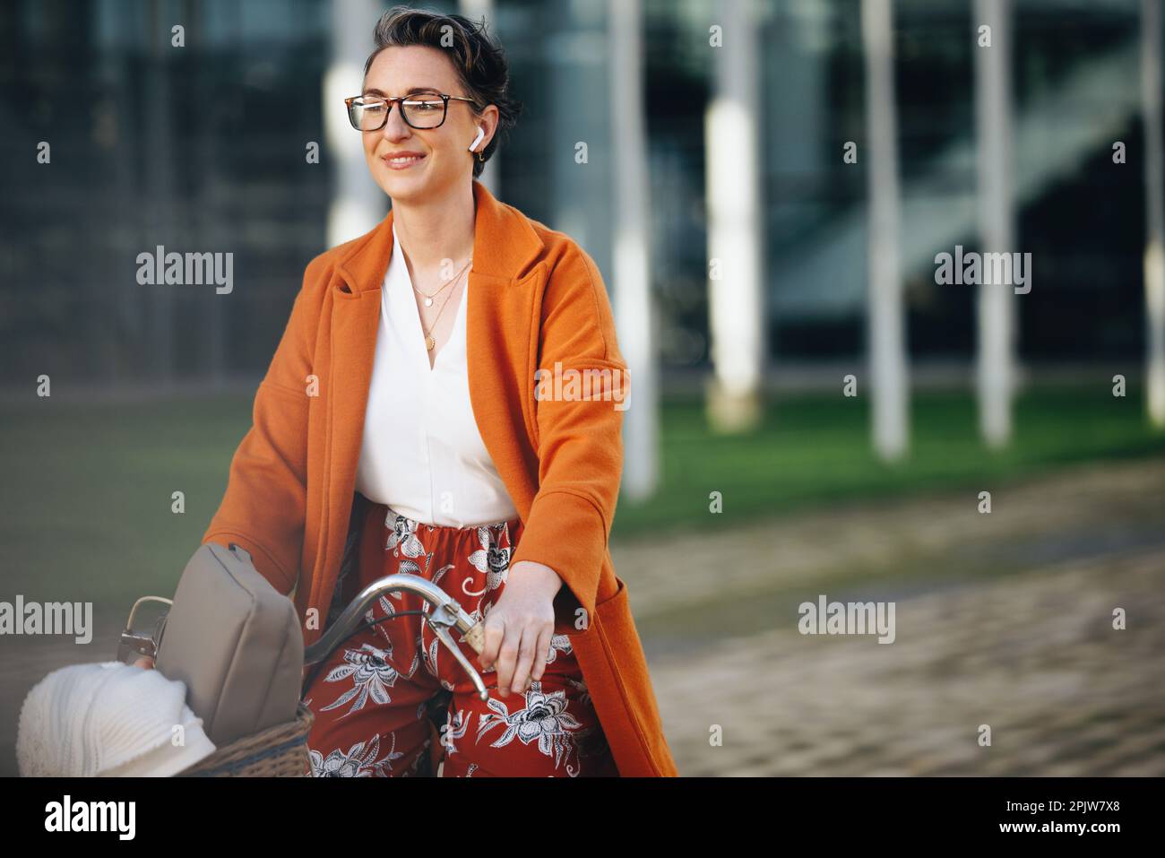 Mature business woman riding a bike and listening to music on her way to work in the morning. Happy business woman commuting to her office in the city Stock Photo