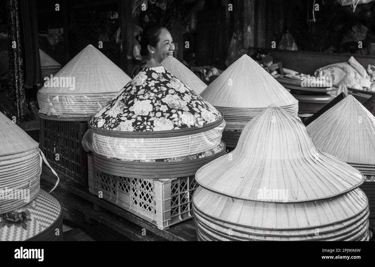 A woman laughs as she sits at her stall selling traditional concial hats in Pleiku Central Market, Vietnam. Stock Photo