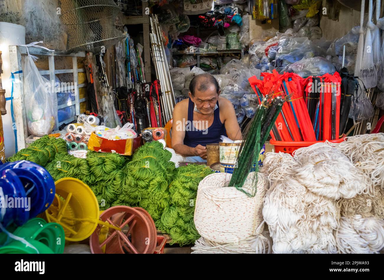 A stallholder sits at his stall selling rope and fishing gear in Pleiku central market in Vietnam. Stock Photo