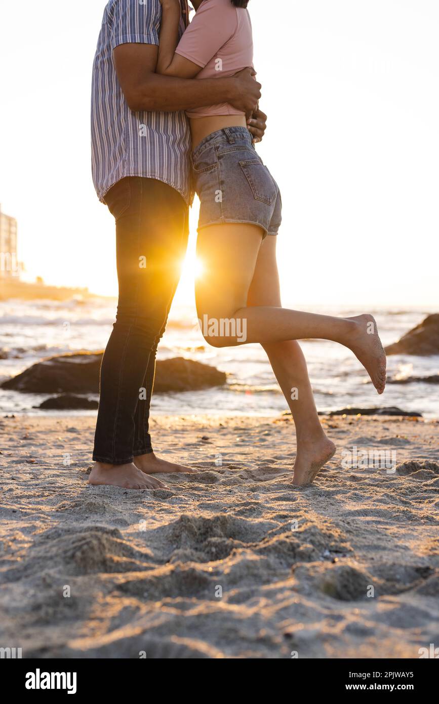 Midsection of happy diverse couple embracing at beach during sunset Stock Photo