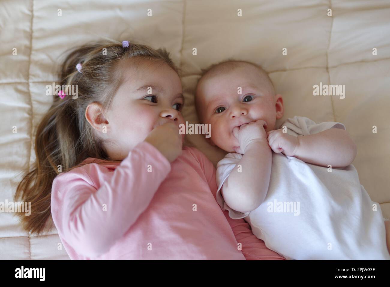 Little girl lying on bed next to her baby brother Stock Photo