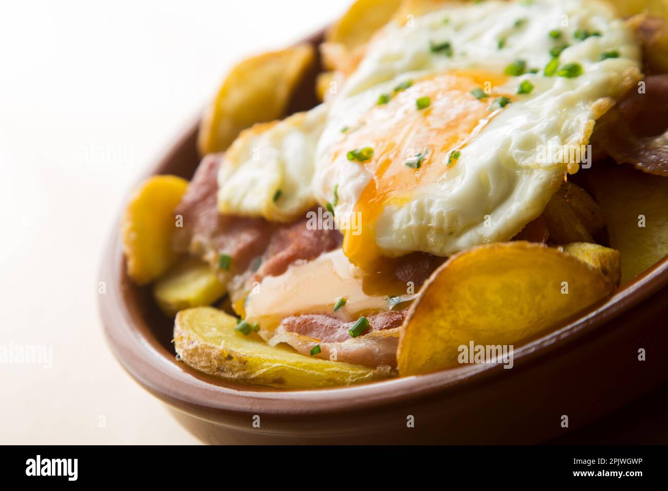 Fried eggs with chips and serrano ham. Traditional Spanish tapa nicknamed Huevos Rotos. Stock Photo