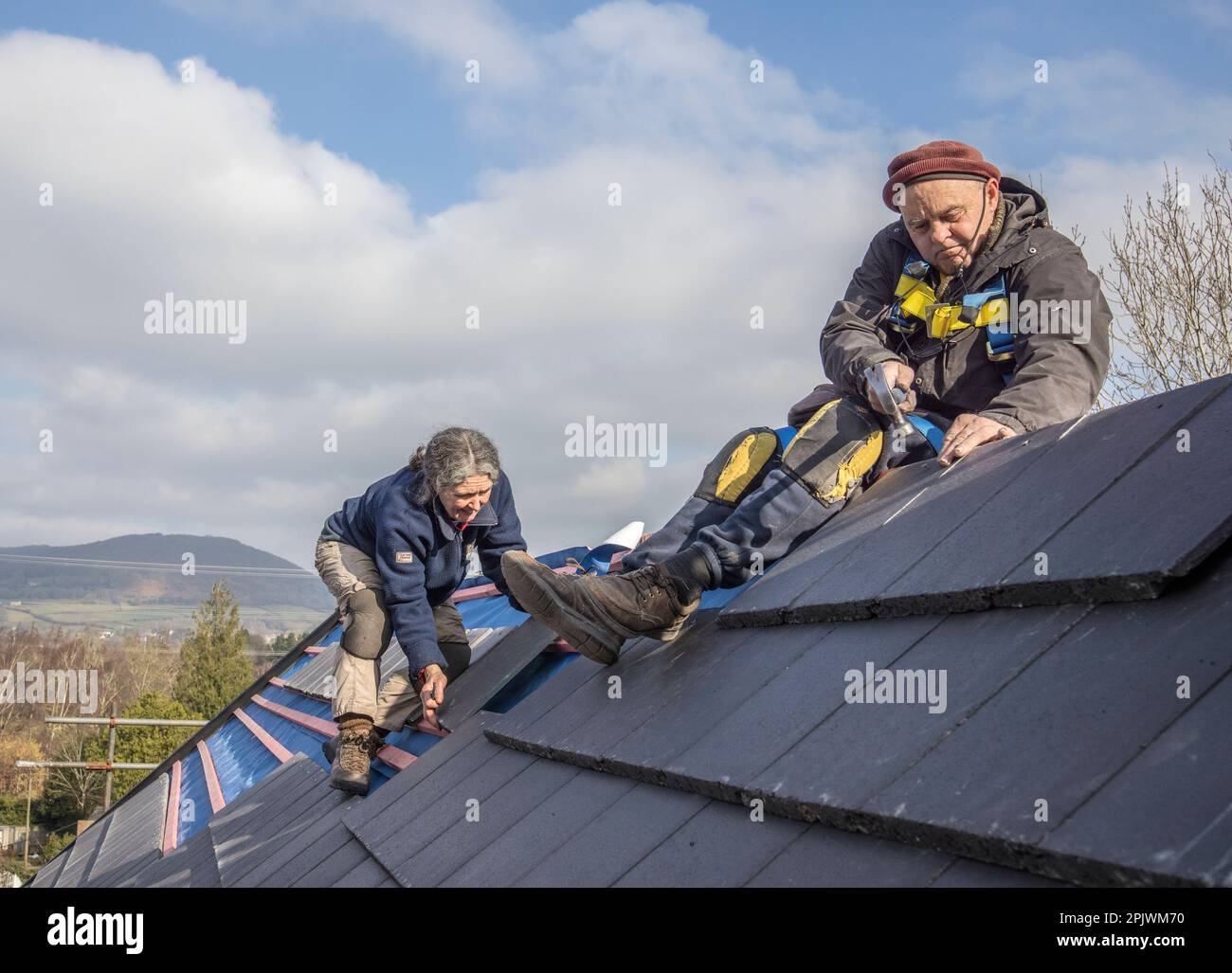 Roofer and assistant working on the ridge fixing new replacement tiles on a house, Llanfoist, Wales, UK Stock Photo