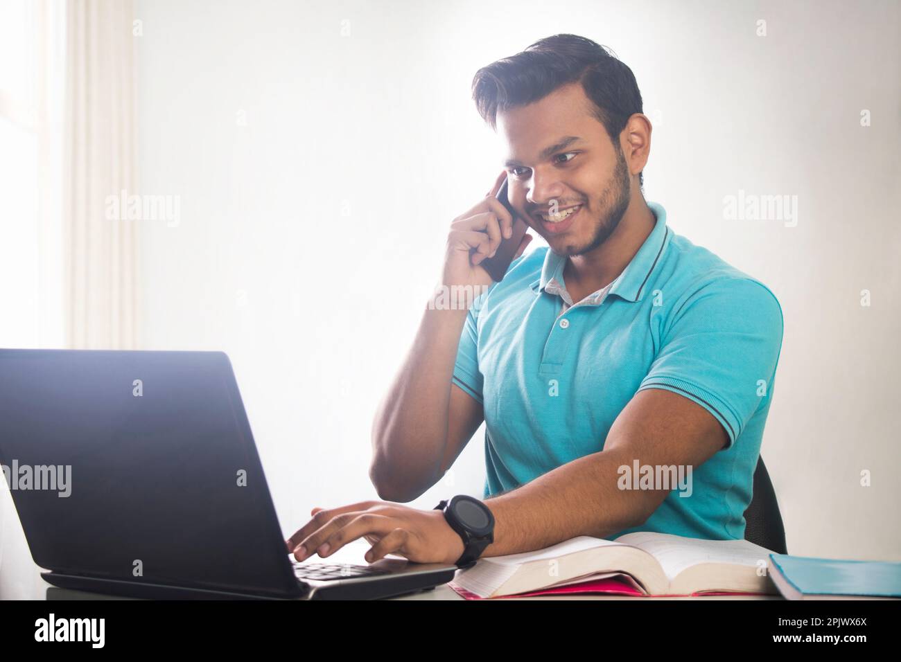 A YOUNG TEENAGER TALKING ON THE PHONE WHILE ATTENDING A CLASS ONLINE Stock Photo