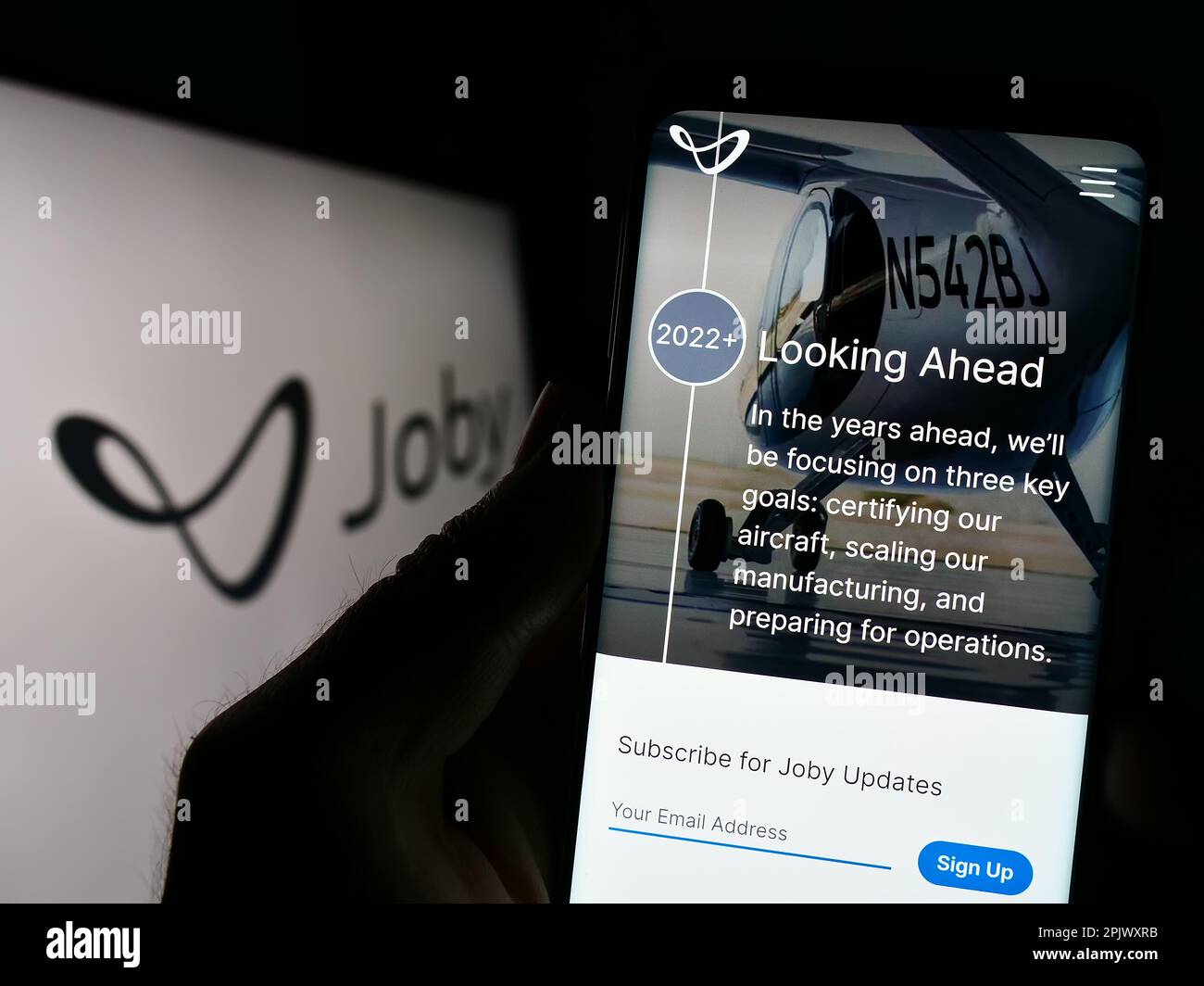 Person holding cellphone with webpage of US eVTOL company Joby Aviation on screen in front of business logo. Focus on center of phone display. Stock Photo