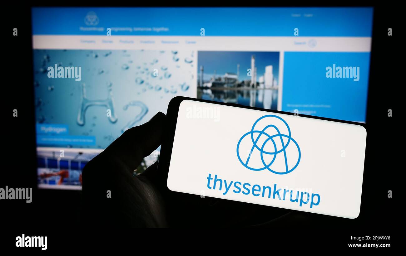 Person holding smartphone with logo of German conglomerate ThyssenKrupp AG on screen in front of website. Focus on phone display. Stock Photo
