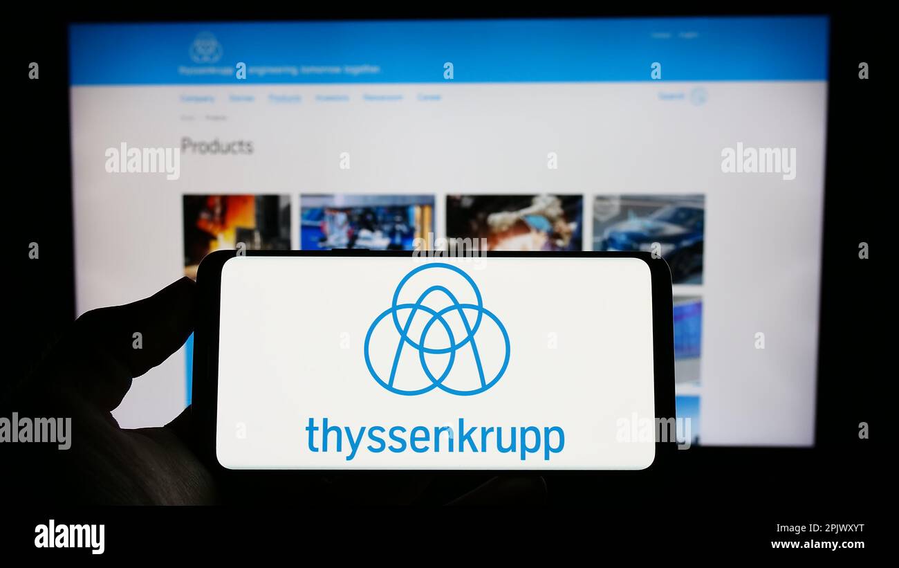 Person holding mobile phone with logo of German conglomerate ThyssenKrupp AG on screen in front of company web page. Focus on phone display. Stock Photo