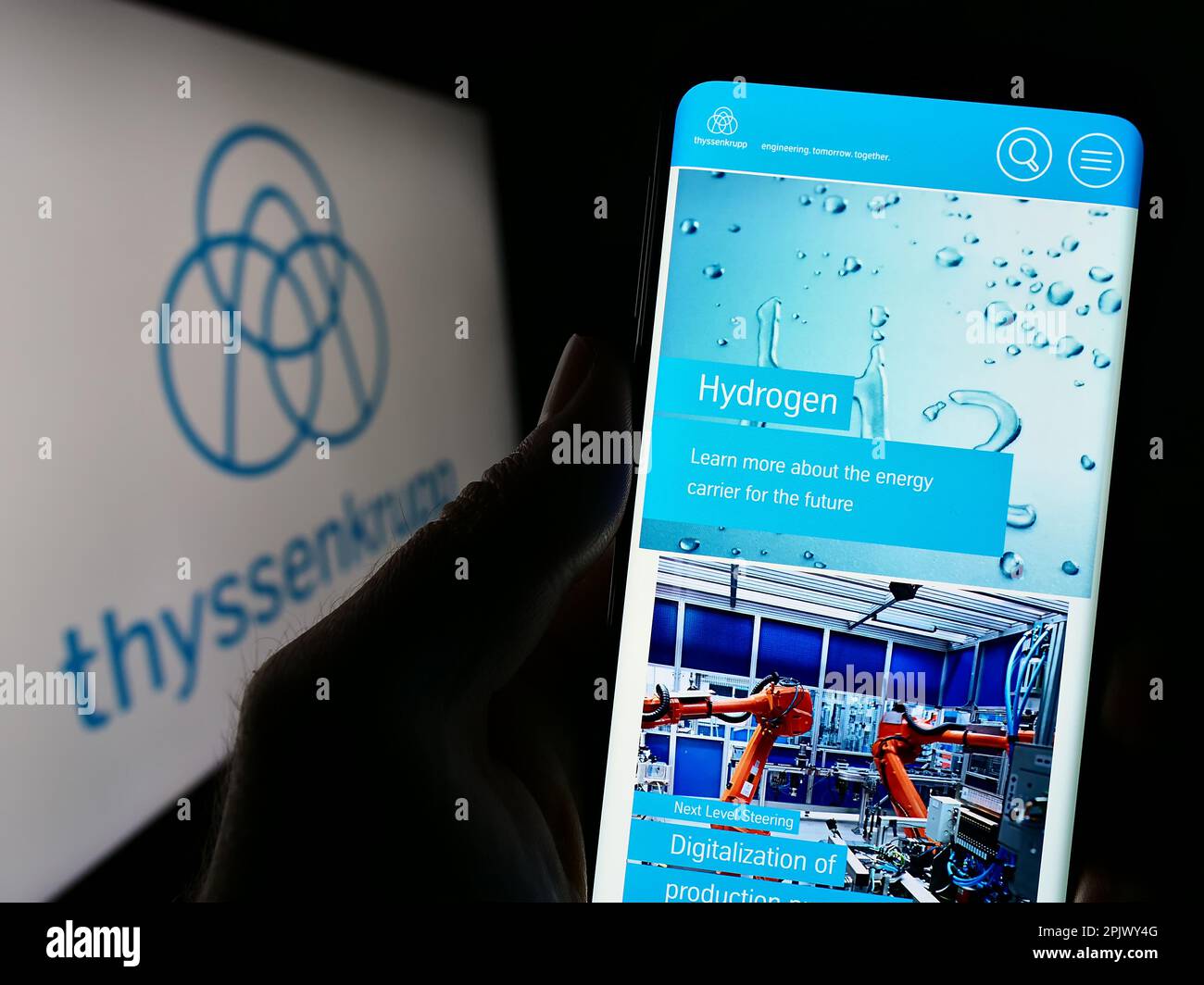 Person holding smartphone with website of German conglomerate ThyssenKrupp AG on screen in front of logo. Focus on center of phone display. Stock Photo