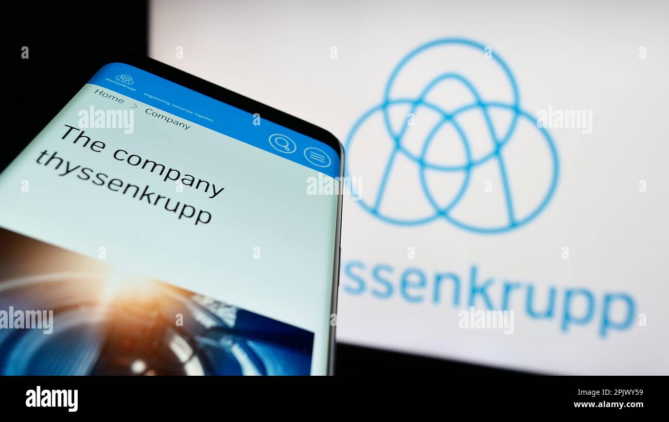 Mobile phone with web page of German conglomerate ThyssenKrupp AG on screen in front of business logo. Focus on top-left of phone display. Stock Photo