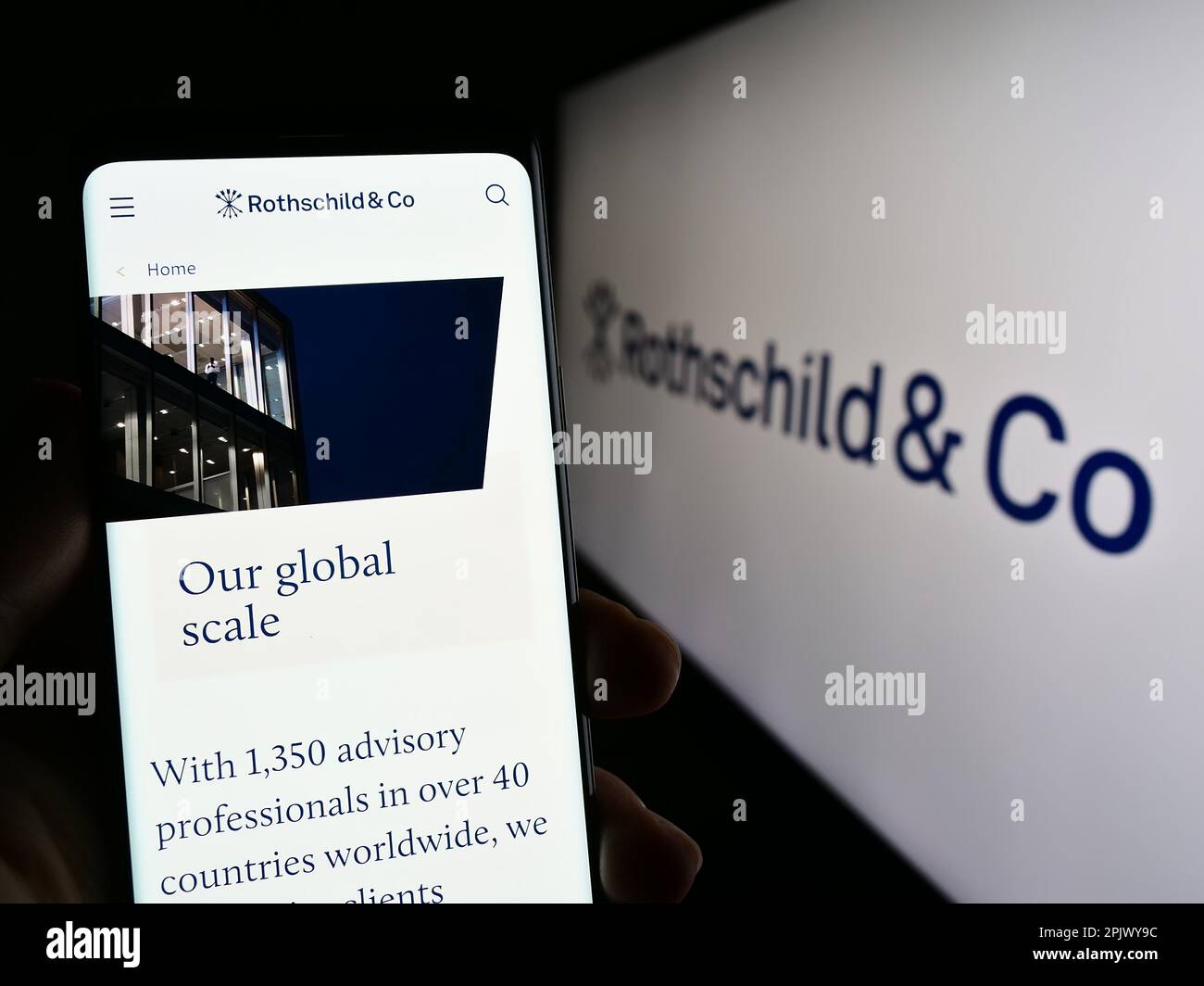 Person holding smartphone with webpage of financial services company Rothschild Co on screen in front of logo. Focus on center of phone display. Stock Photo