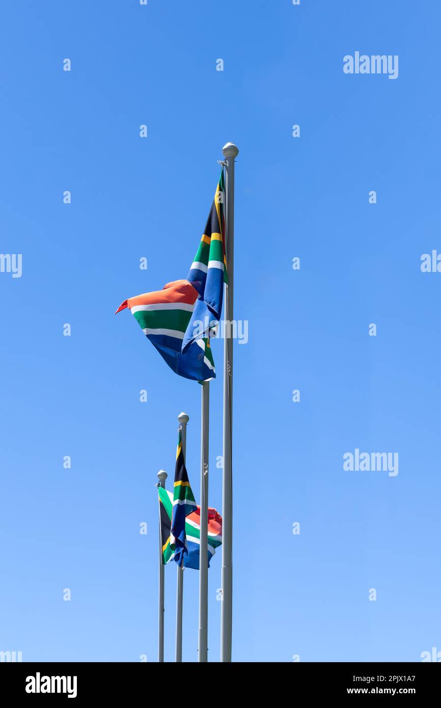 3 flags of South Africa waving in the wind against a blue sky background Stock Photo