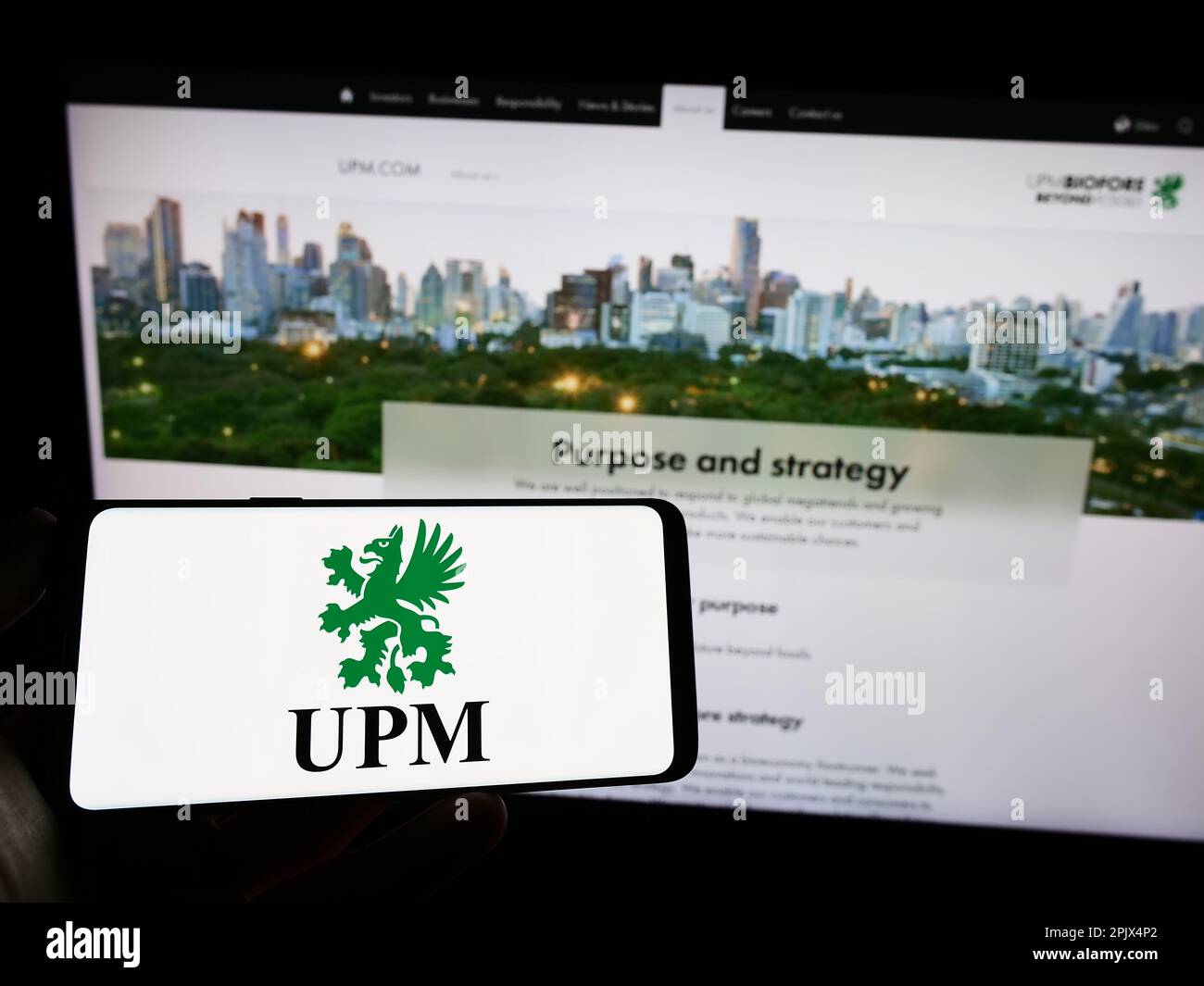 Person holding mobile phone with logo of Finnish forestry company UPM-Kymmene Oyj on screen in front of business web page. Focus on phone display. Stock Photo