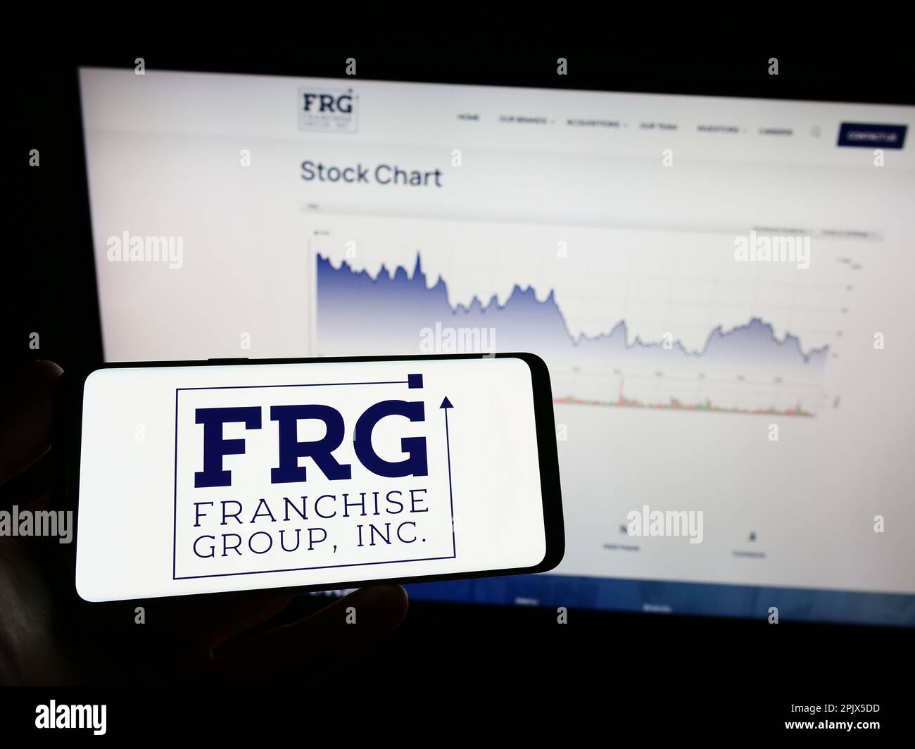 Person holding mobile phone with logo of American company Franchise Group Inc. (FRG) on screen in front of web page. Focus on phone display. Stock Photo