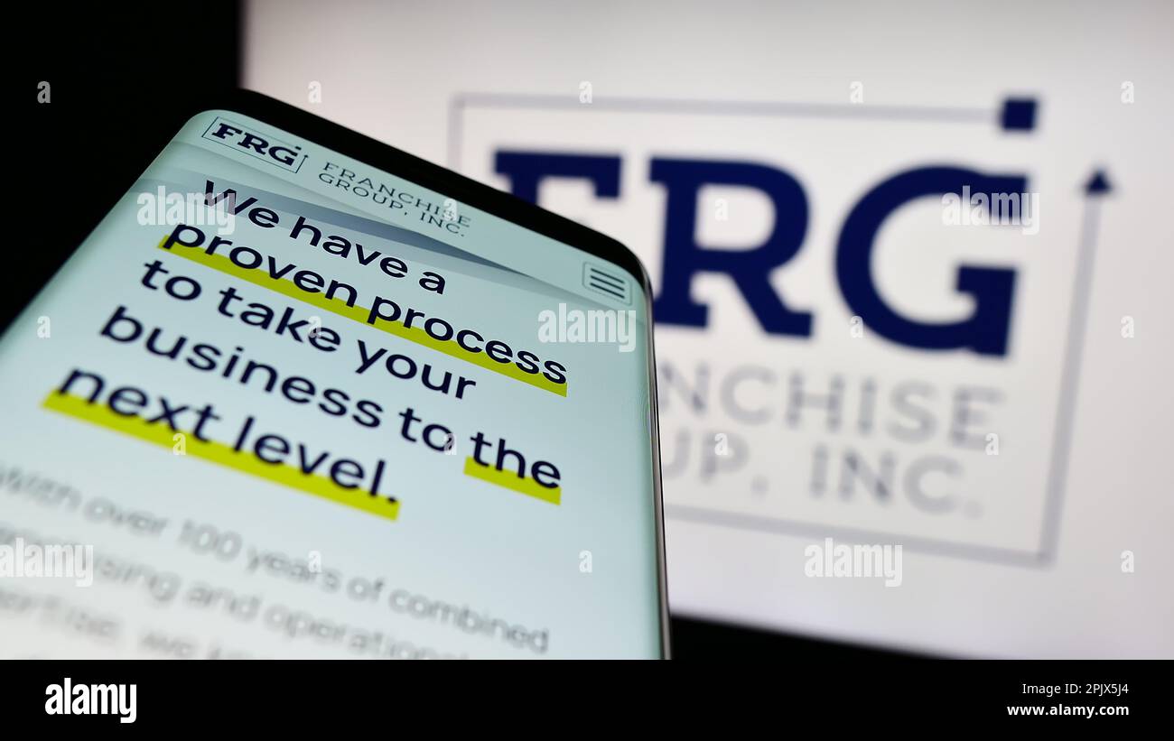 Smartphone with website of US company Franchise Group Inc. (FRG) on screen in front of business logo. Focus on top-left of phone display. Stock Photo