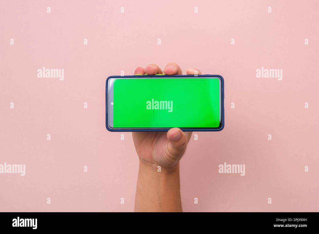 Human hand holding mobile smartphone with green screen in horizontal position isolated on pink background. Stock Photo