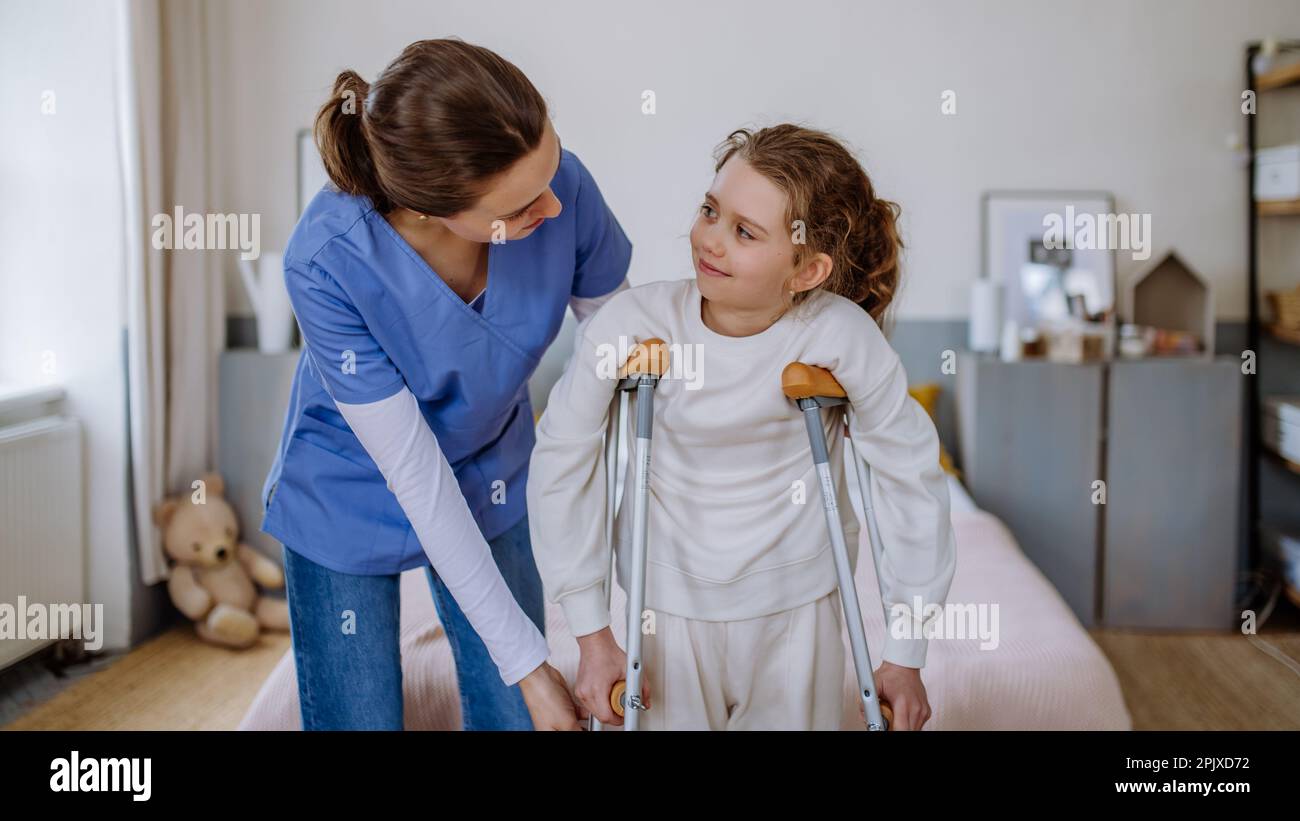 Young nurse helping to walk to little girl with broken leg Stock Photo