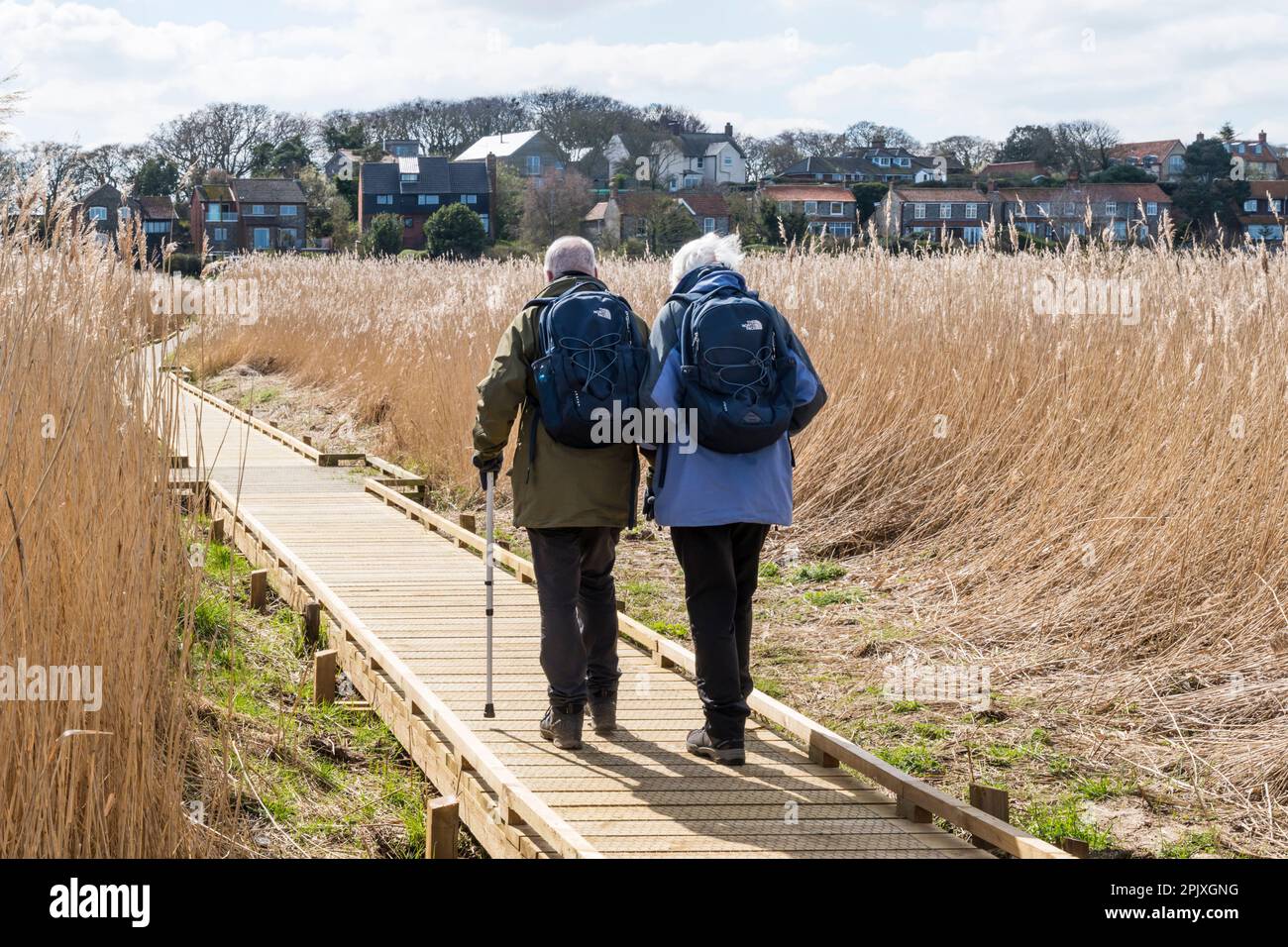 An active senior couple on a boardwalk through the reeds at Cley Marshes nature reserve of Norfolk Wildlife Trust. Stock Photo