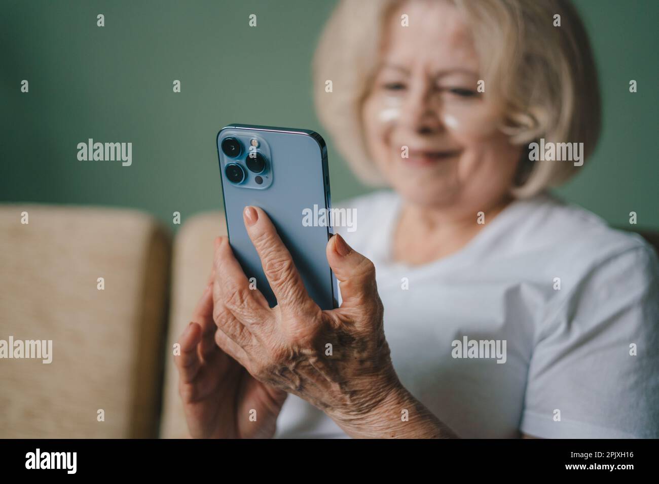 Pretty, old woman enjoying her skincare routine in living room with eye