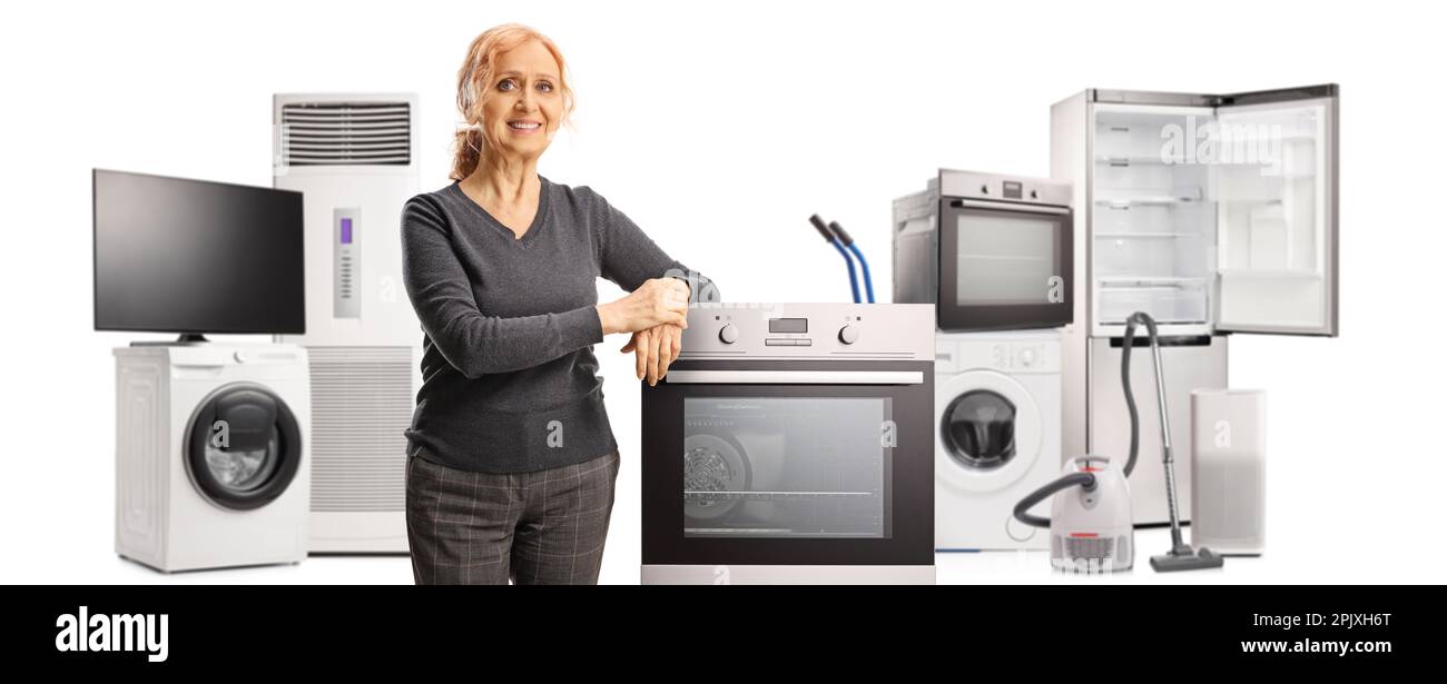 Smiling mature woman leaning on an oven and other home applances in the back isolated on white background Stock Photo