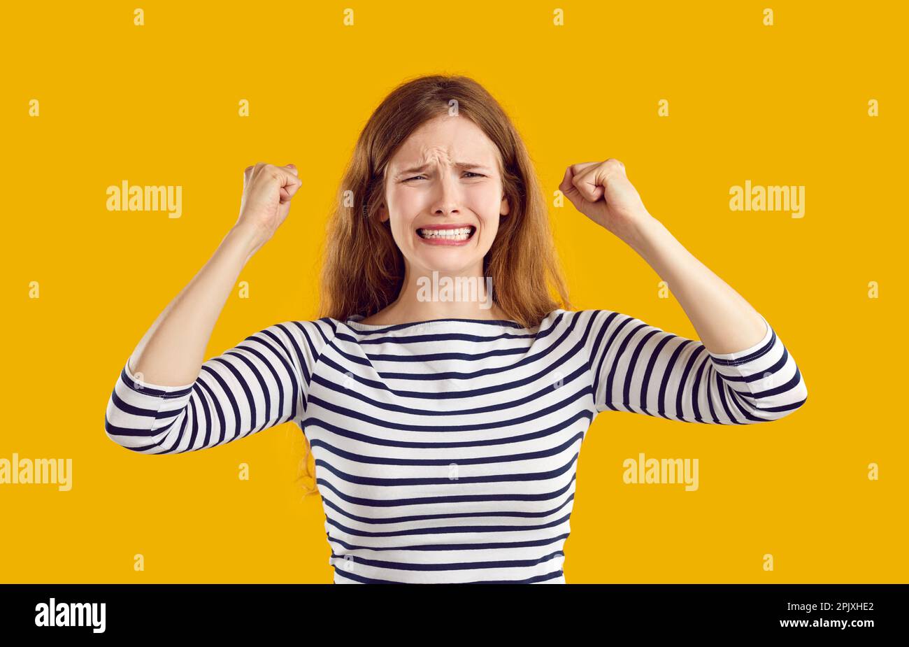 Young sad confused frustrated woman in trouble clenches her fists in despair on yellow background. Stock Photo