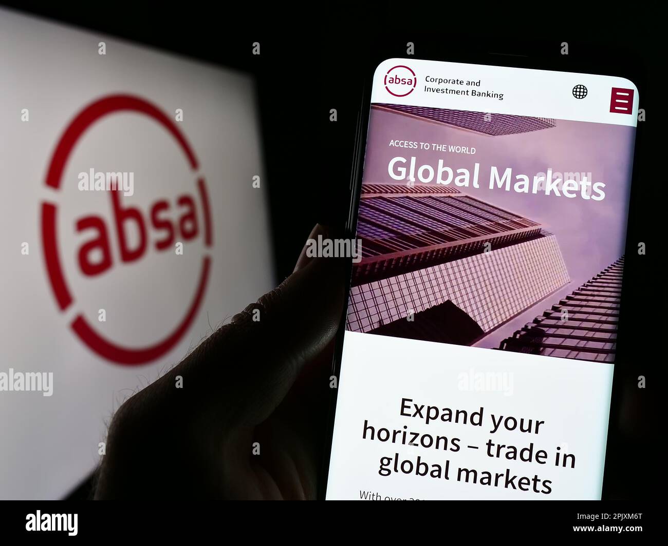 Person holding cellphone with webpage of South African company Absa Group Limited on screen in front of logo. Focus on center of phone display. Stock Photo