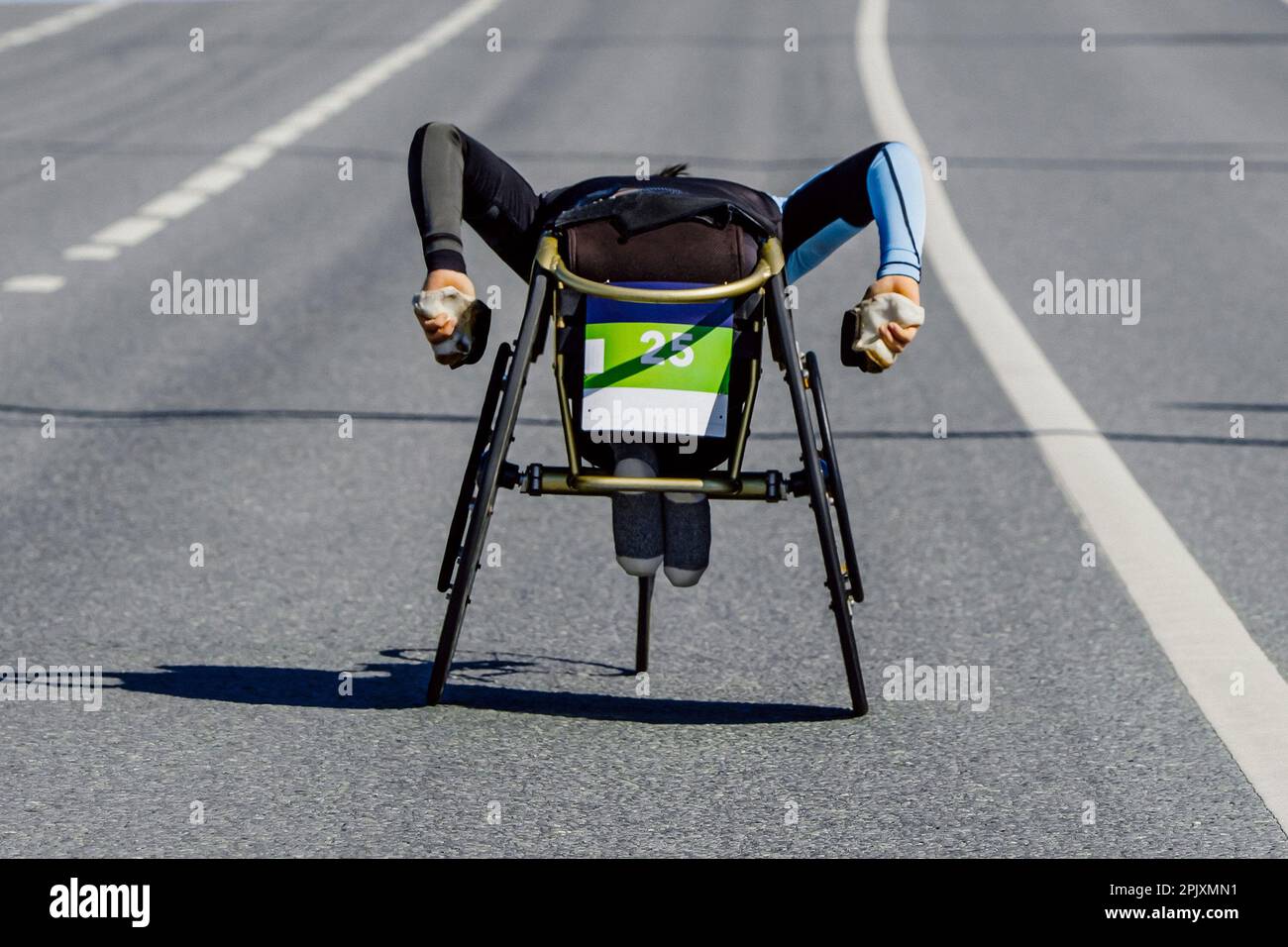 para athlete in wheelchair riding road marathon race, movement uphill overpass, para athletics competition Stock Photo