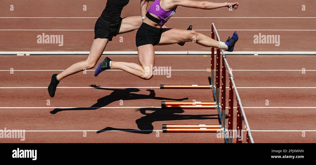 two female athletes running hurdles in athletics competition, hurdling