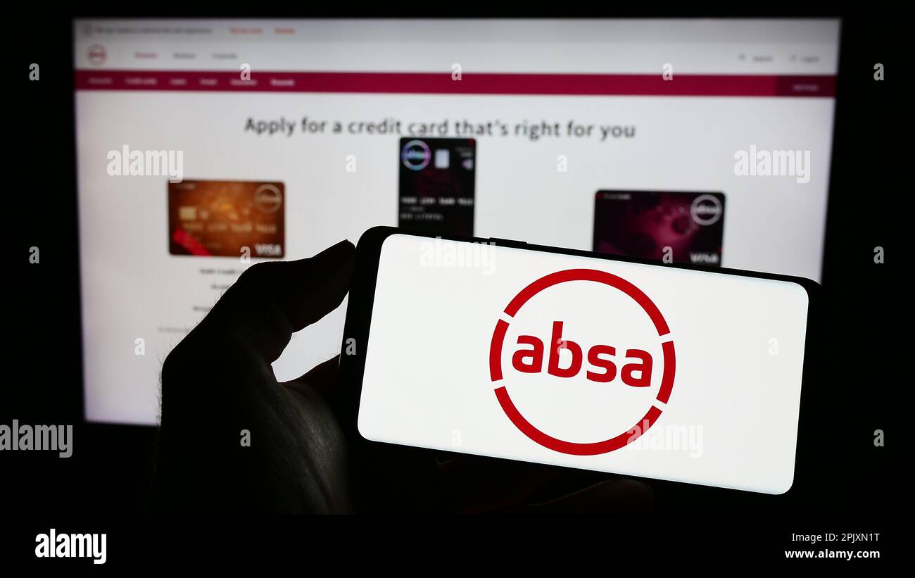 Person holding mobile phone with logo of South African company Absa Group Limited on screen in front of business web page. Focus on phone display. Stock Photo