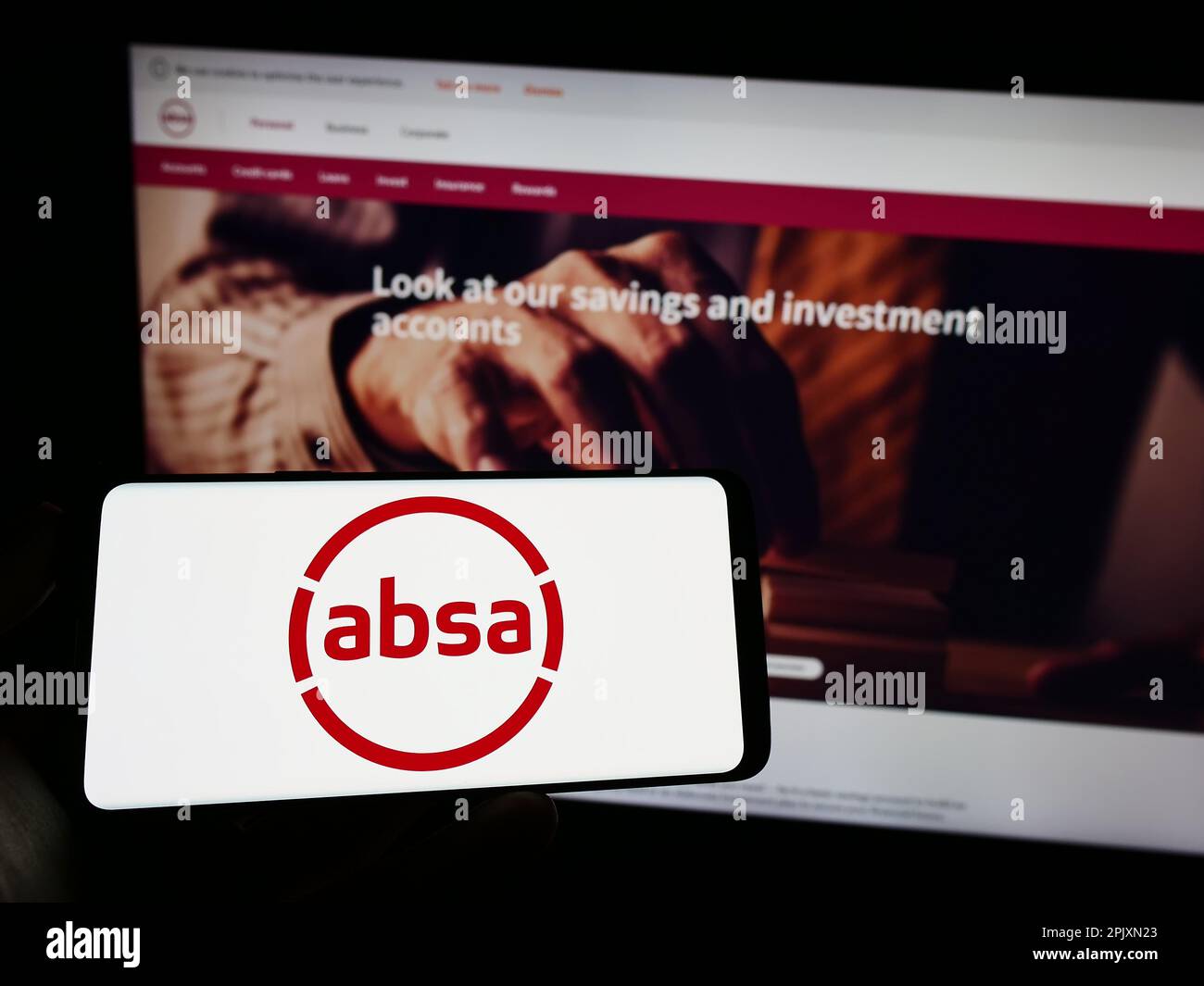 Person holding cellphone with logo of South African company Absa Group Limited on screen in front of business webpage. Focus on phone display. Stock Photo