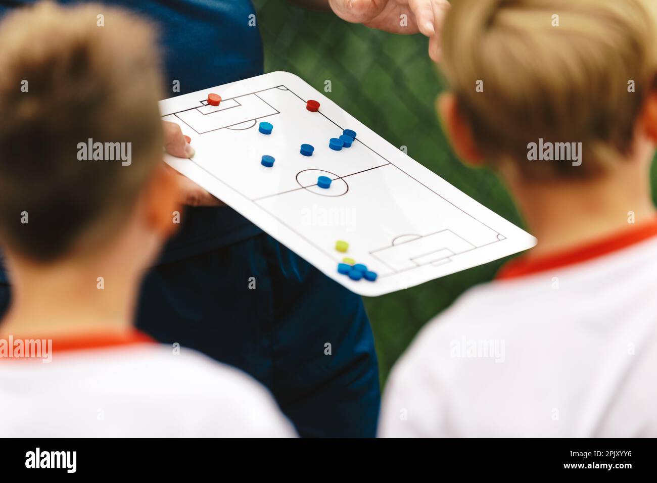 A young coach explains to a group of children the soccer team strategy using a tactics board. School coach coaching kids in a sports team. Strategy bo Stock Photo