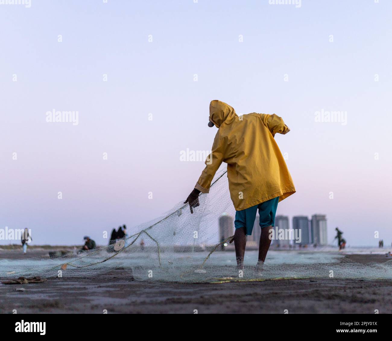karachi pakistan 2021, a fisherman wearing yellow jacket preparing fishing net for fishing at