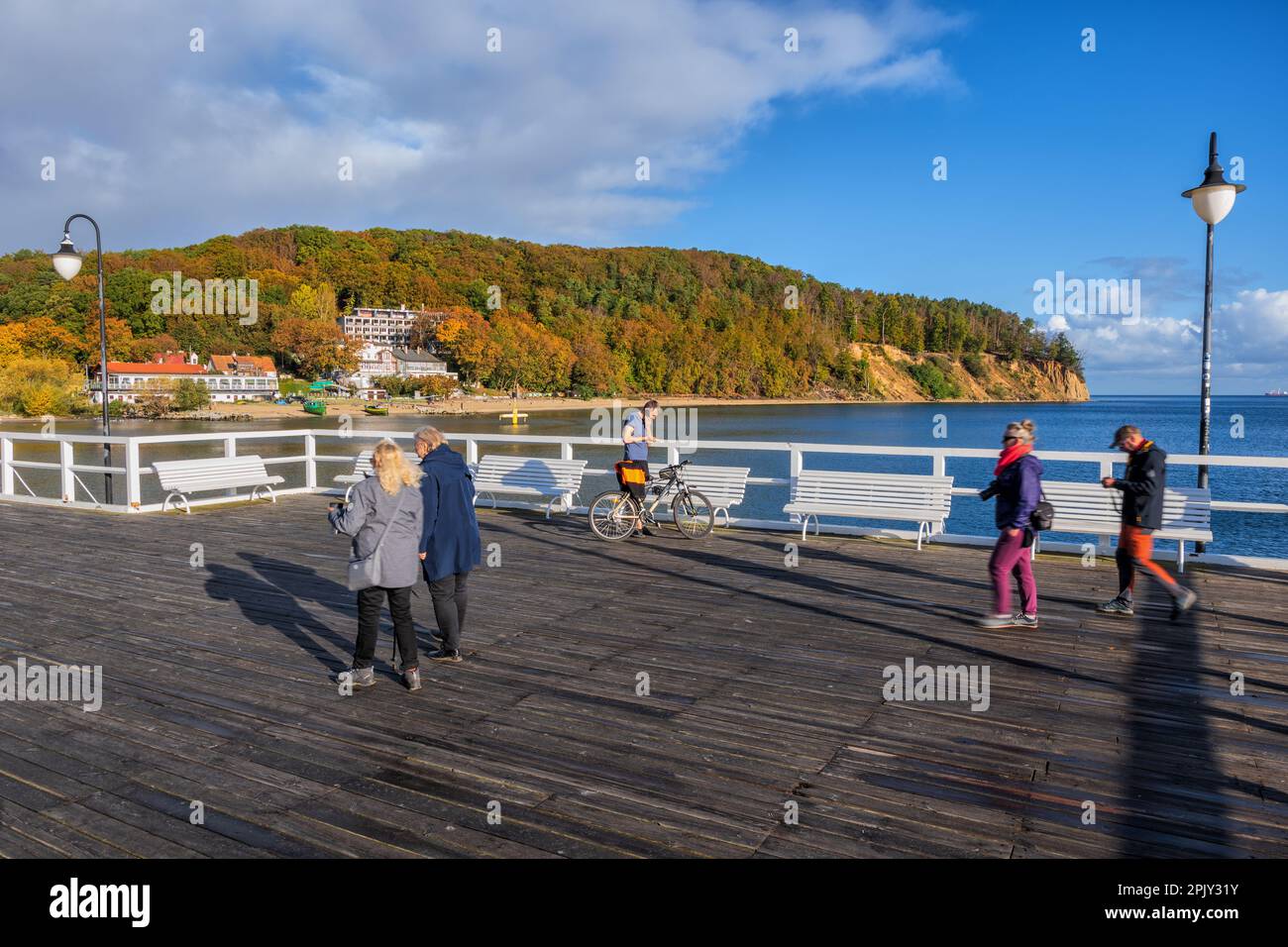 People on wooden Orlowo Pier on the Baltic Sea in Gdynia, Poland with view to the Orlowski Cliff in autumn. Stock Photo