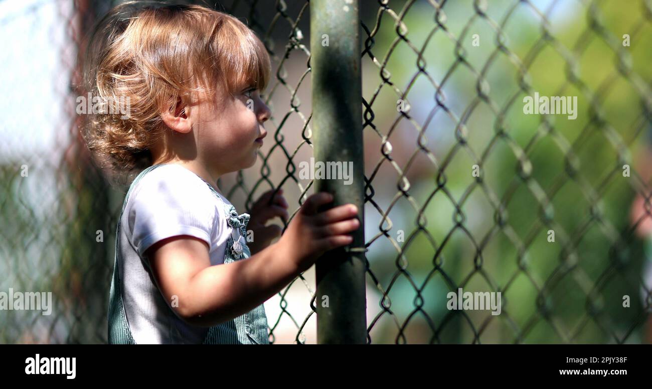 Contemplative little boy watching game match through fence. Infant boy watches sport event Stock Photo