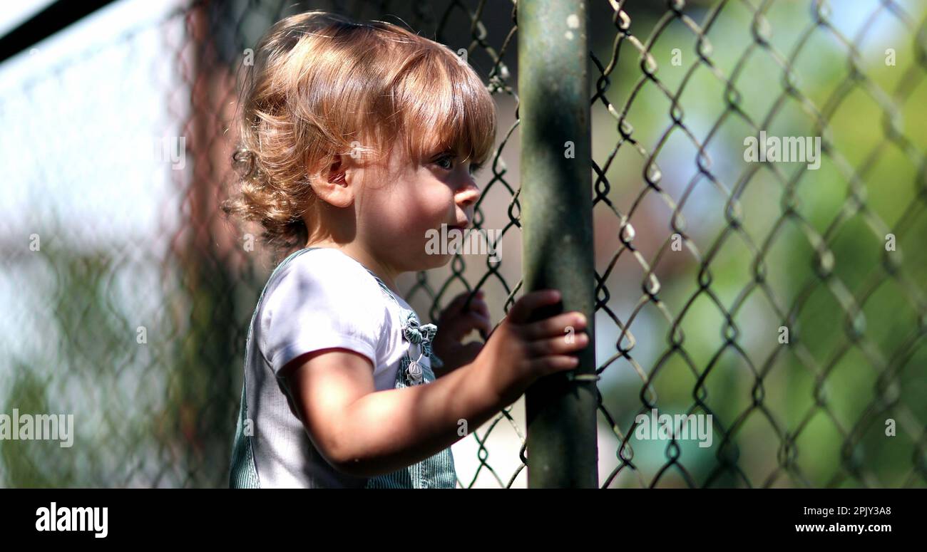 Contemplative little boy watching game match through fence. Infant boy watches sport event Stock Photo