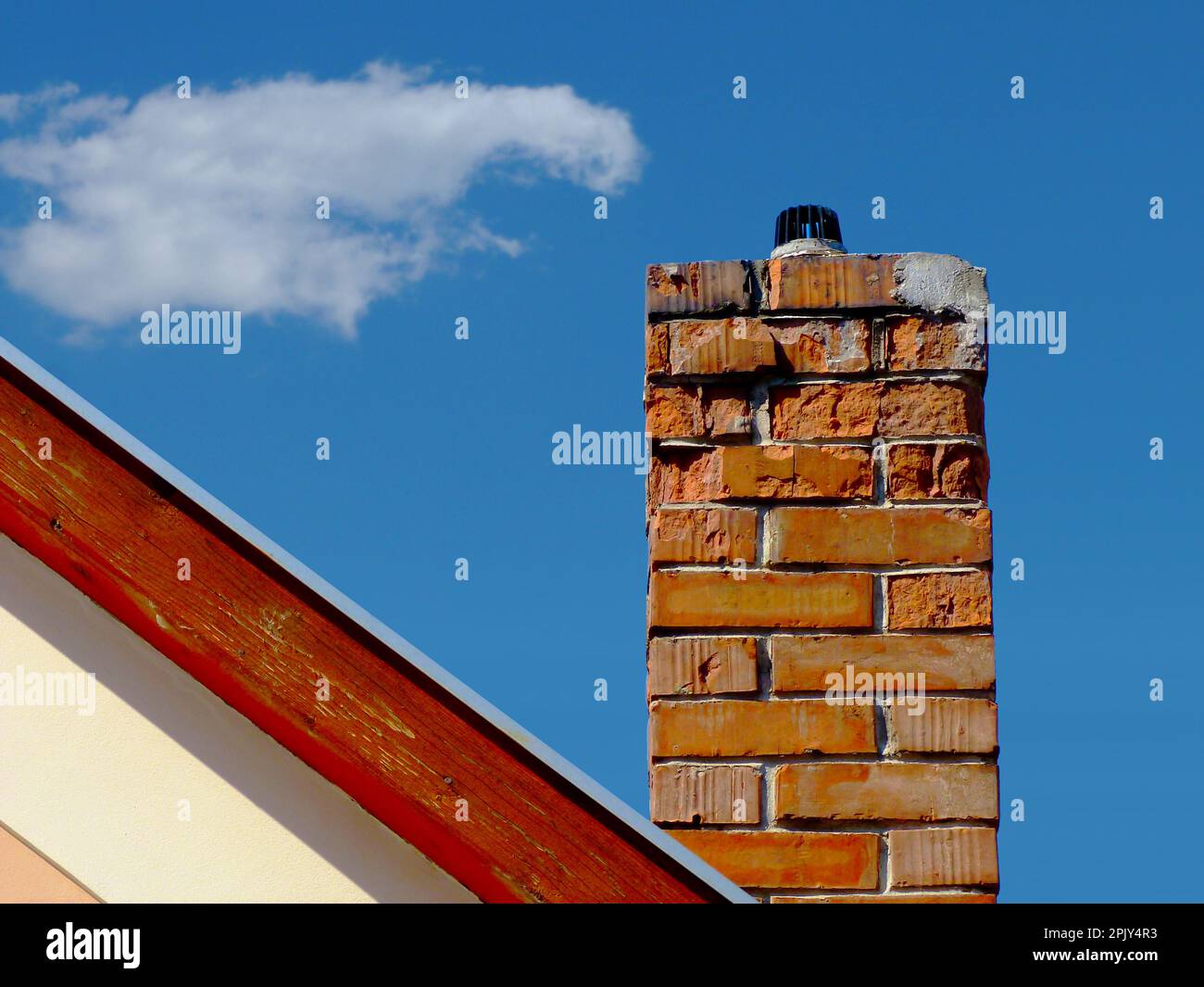 Isolated deteriorating clay brick chimney with weathered, spalling surface. wood trim on house