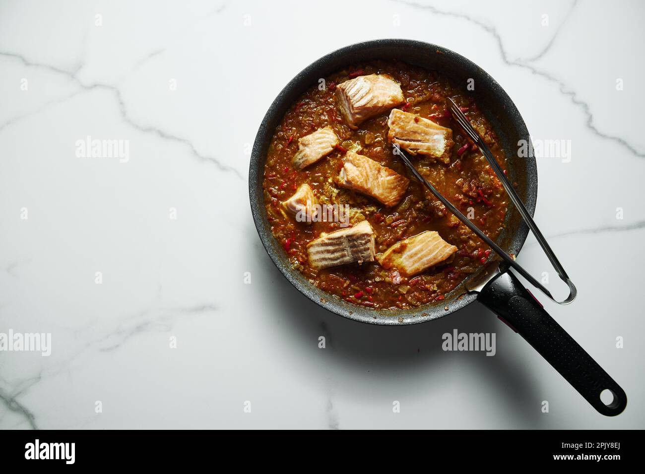 Frying pan with Indian salmon curry dish. Fried salmon fillets, stewed