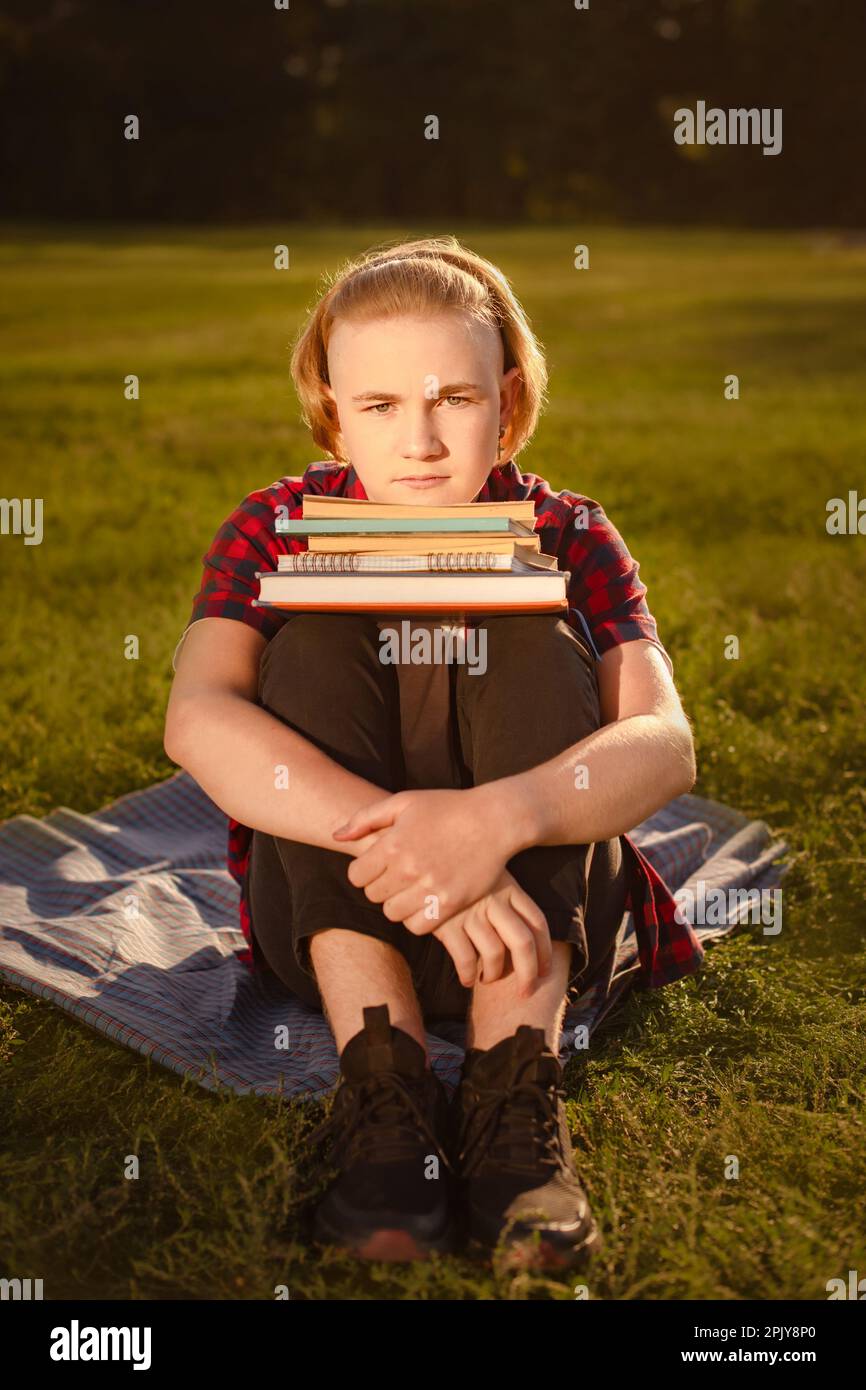 student boy study in green park, sitting on green grass with stack of books and looking at camera. ready to pass exams Stock Photo
