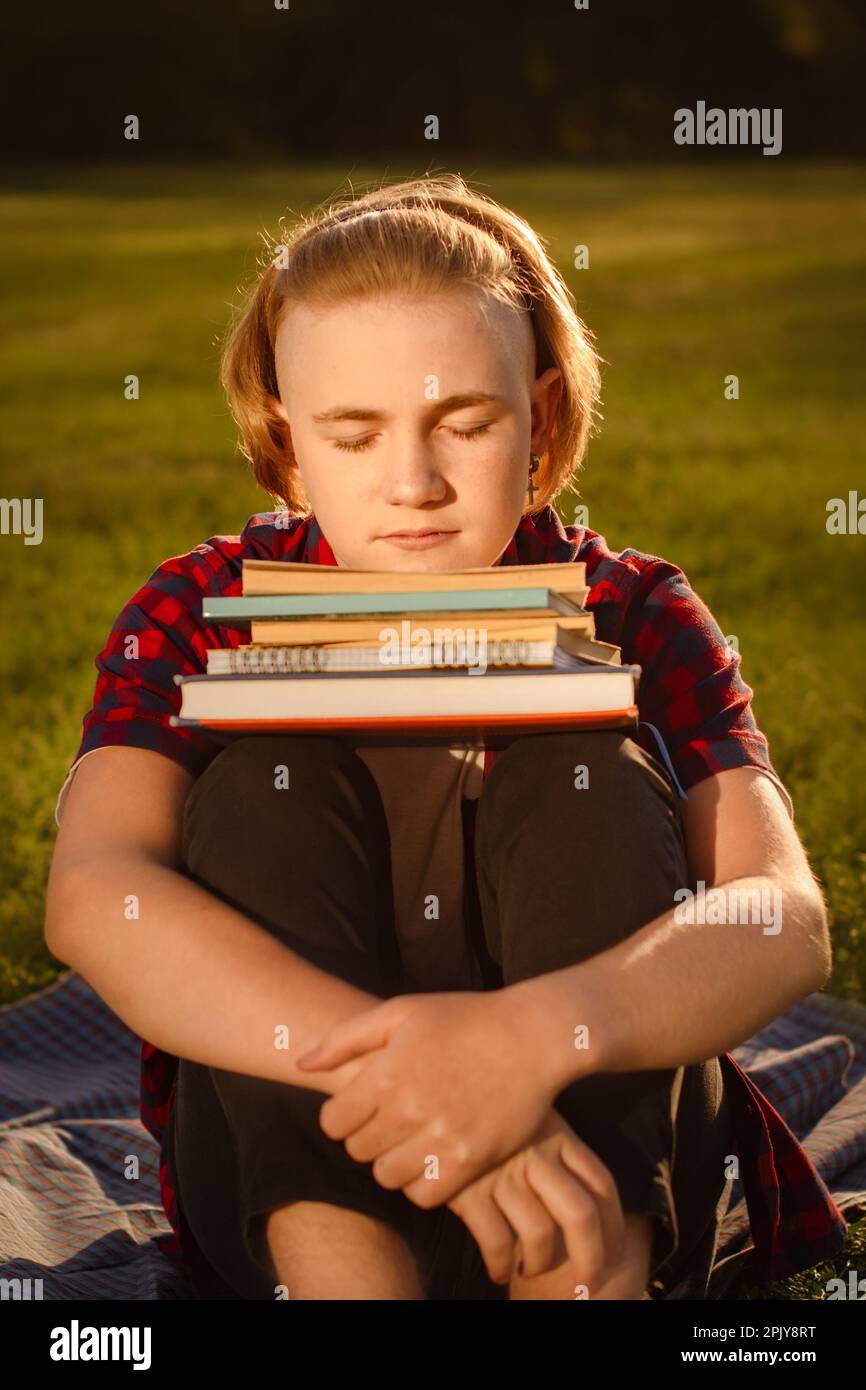 teenager boy study in green park, sitting on green grass with stack of books. preparing pass exams Stock Photo