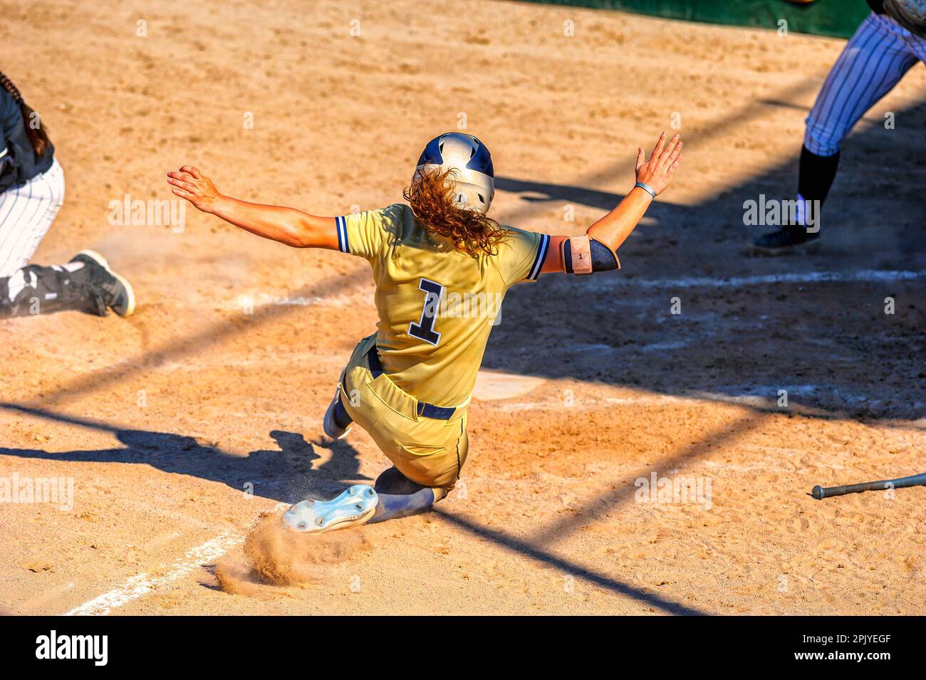A Baseball Softball Player Is Sliding Into Home Plate Stock Photo